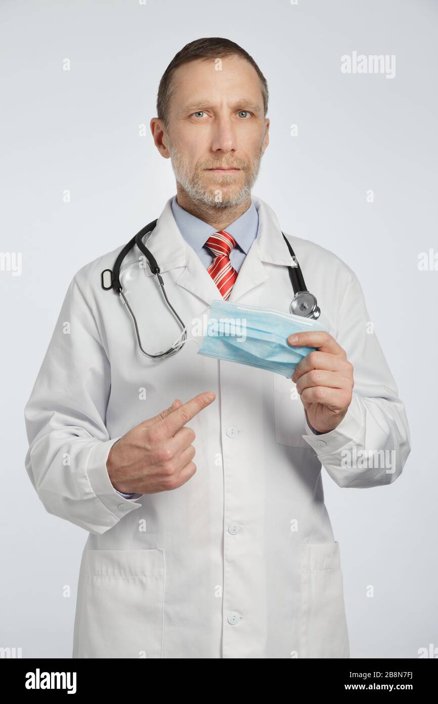 Ein Arzt in einem medizinischen Mantel und ein Stethoskop auf seinen Schultern zeigt eine medizinische Maske Stockfoto