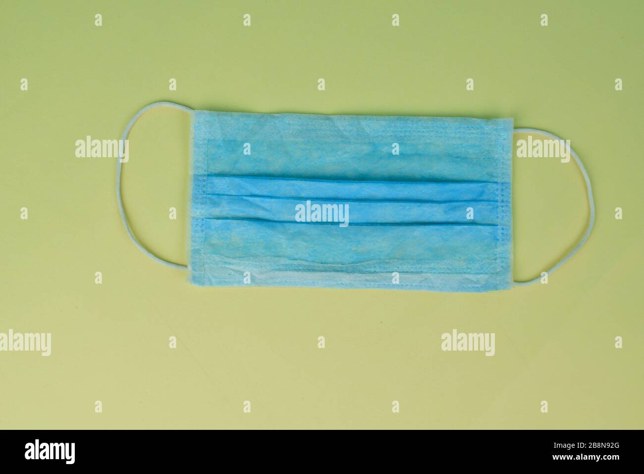 Blaue Operationsmaske mit Gummibändern, isoliert auf hellgelbem Papierhintergrund Stockfoto