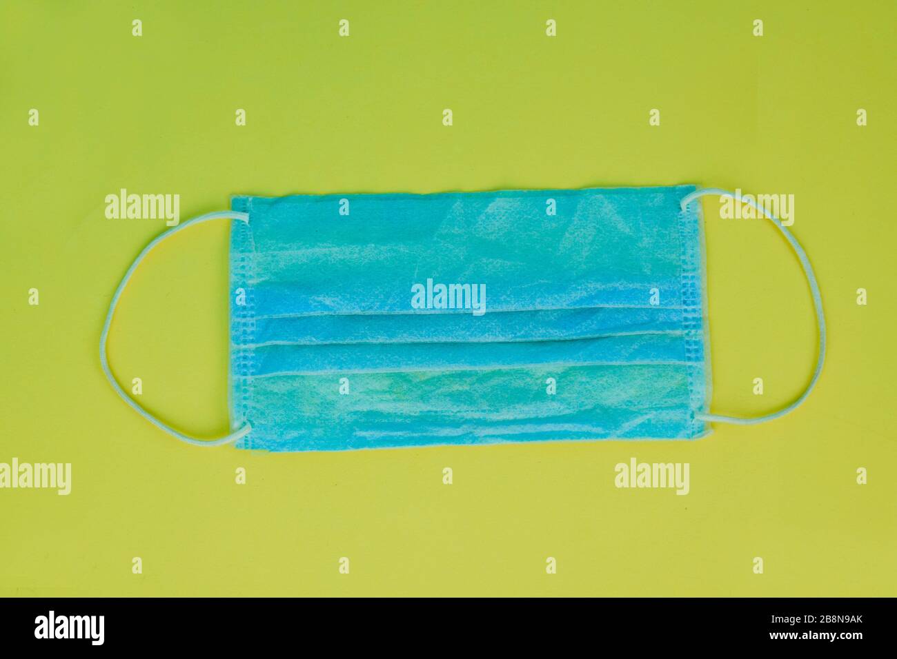Blaue Operationsmaske mit Gummibändern, isoliert auf gelbem Papierhintergrund Stockfoto