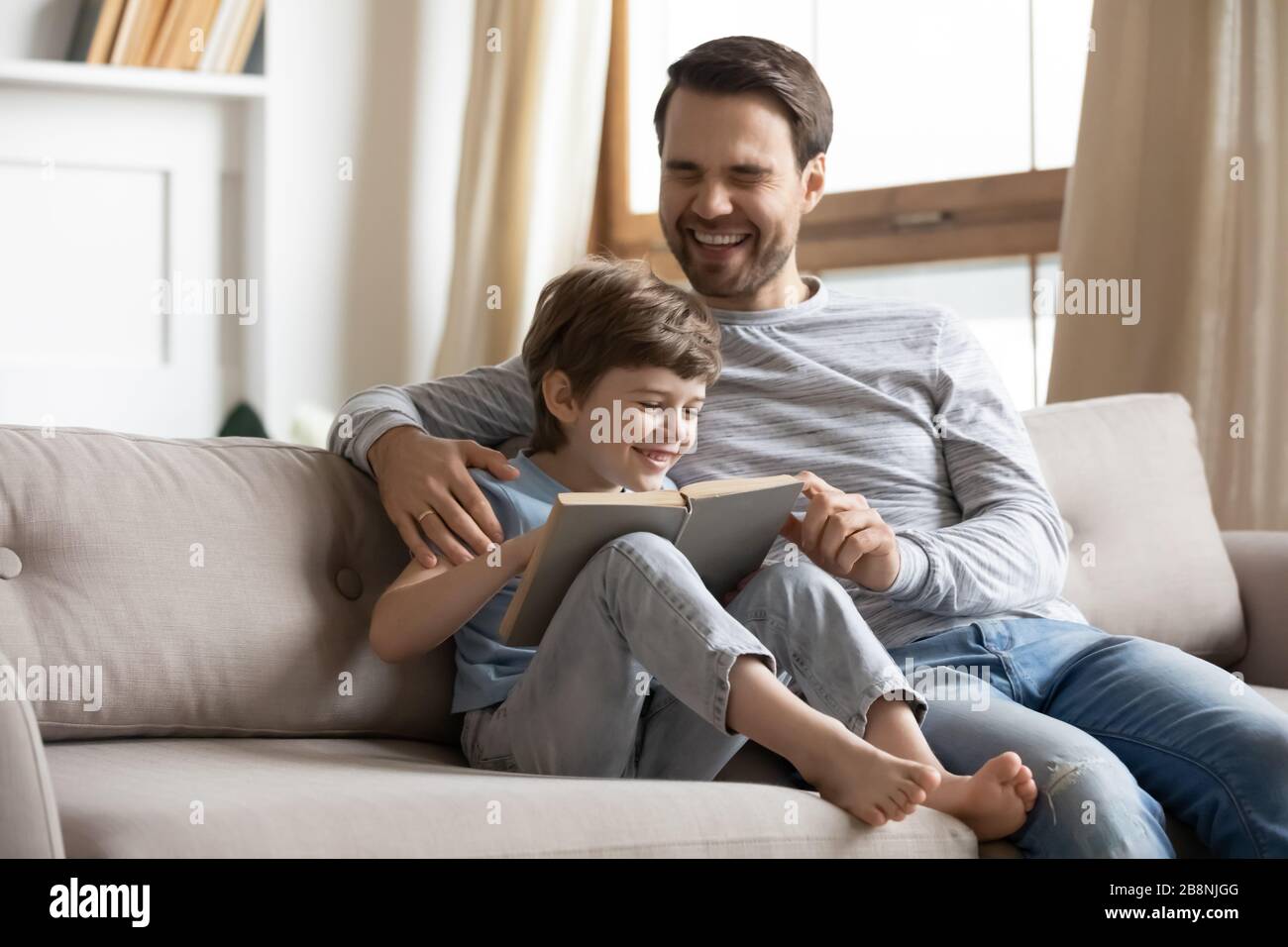 Lächelnder junger Vater und kleiner Sohn lesen Buch zusammen Stockfoto