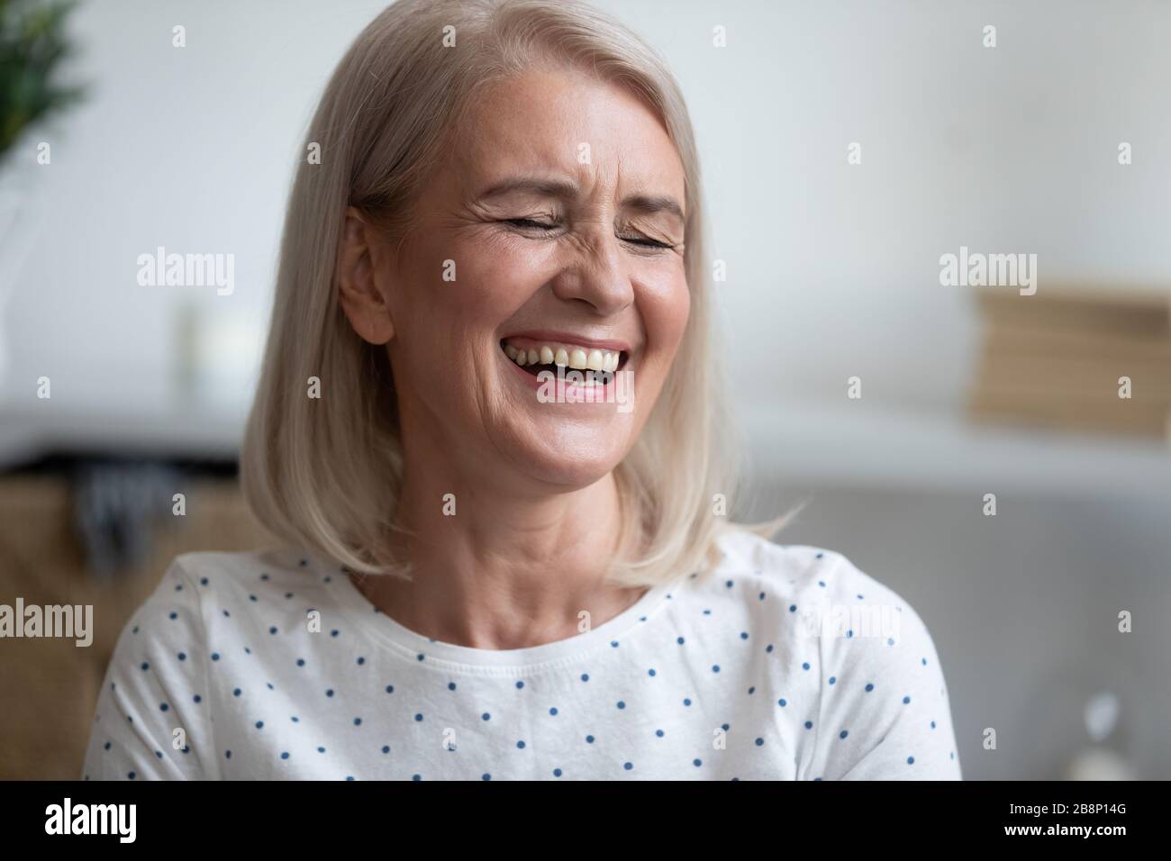 Fröhliche blonde Frau mittleren Alters lacht über lustigen Witz. Stockfoto