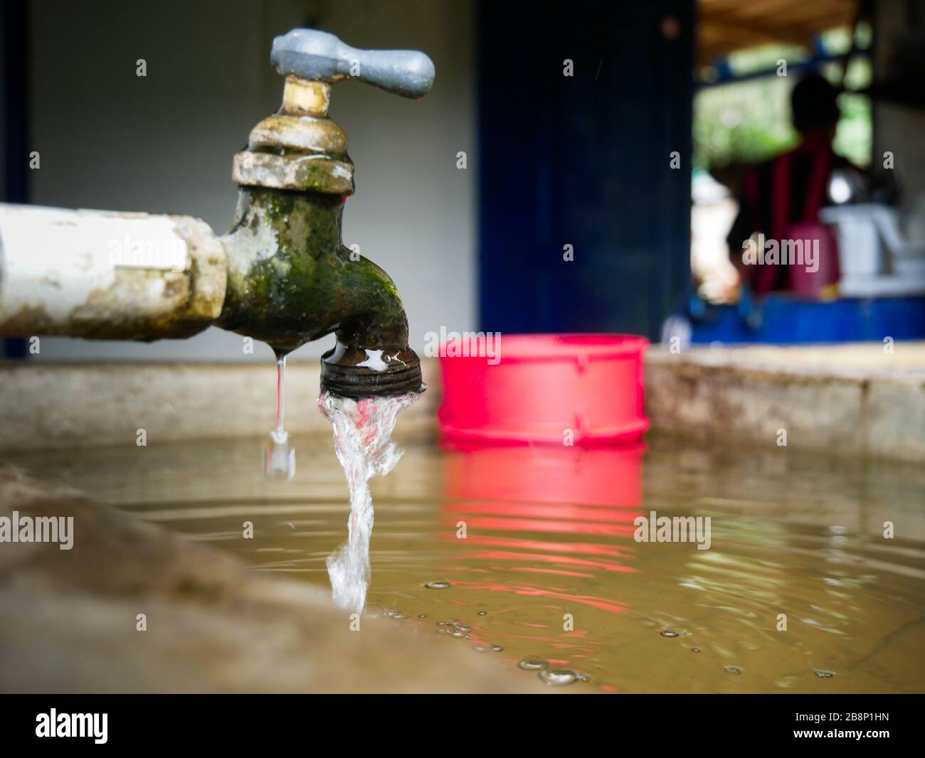 Wasserhahn tropft auf einem Teich in einem ländlichen Haus mit einem Mann im Hintergrund in der Nähe der Stadt Jardin antioquia nachhaltige Entwicklung Ziele Wasser Stockfoto