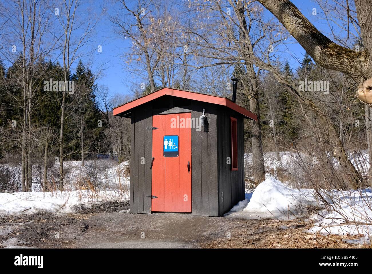 Sehr praktische rote und braune öffentliche unisex-toilette (Outhouse) inmitten eines verschneiten Gatineau Parks, Quebec, Kanada. Stockfoto