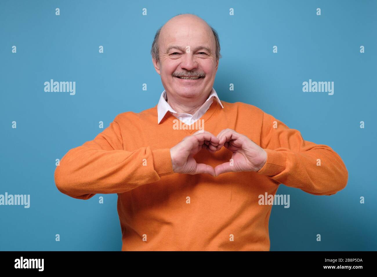 Reifer Mann zeigt Herz mit Fingern im Studio Stockfoto