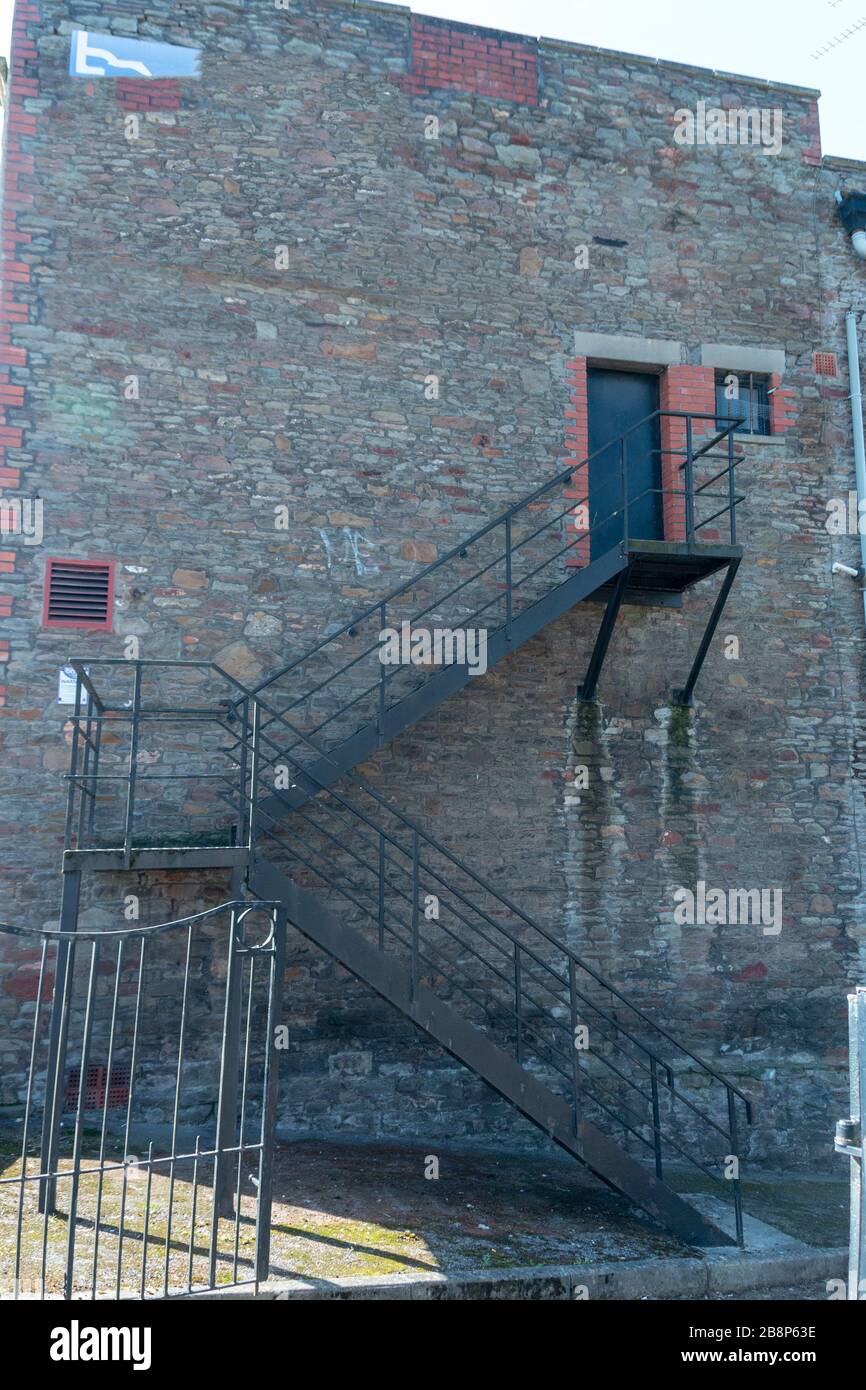 Nahansicht eines Metalltreppentabs, das zu einer massiven schwarzen Tür an der Seite eines Gebäudes führt Stockfoto