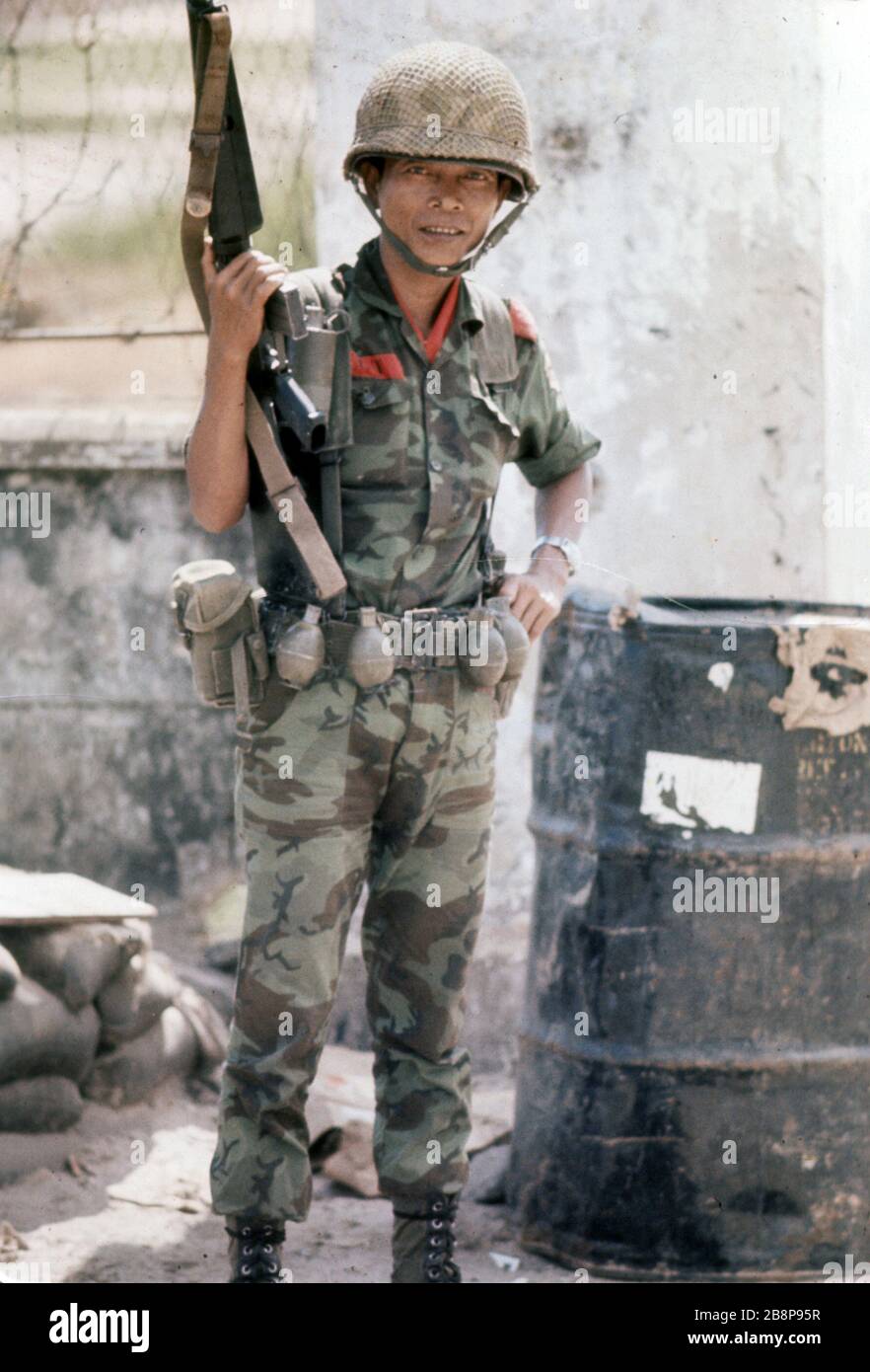 1968, Danang, Vietnam, authentisches Foto eines südvietnamesischen Soldaten, der in Vietnam eine Waffe neben Trommeln mit Chemikalien hält Stockfoto