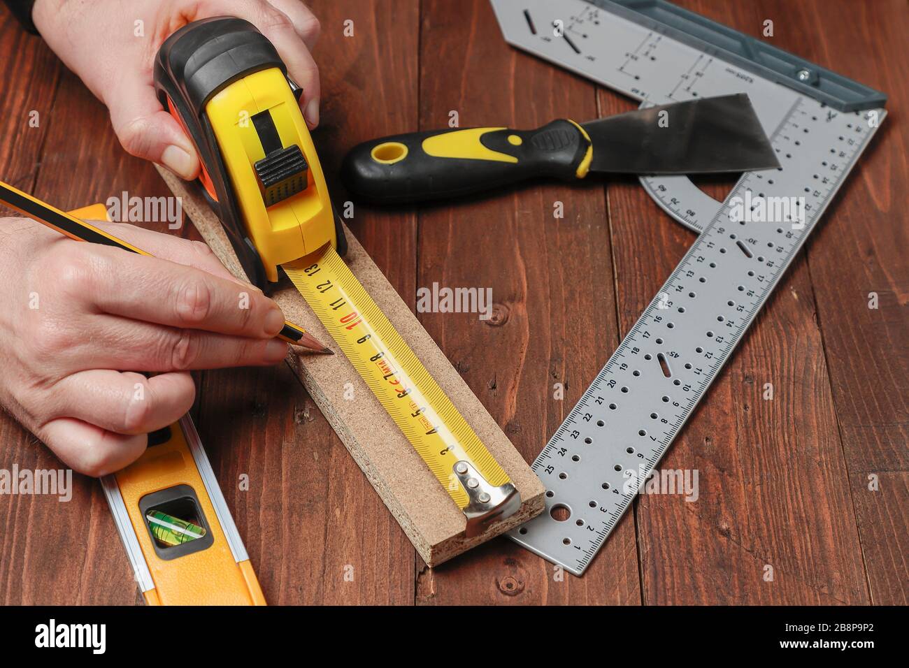 Horizontale Ansicht von oben von zwei Händen mit einem Bleistift und einem Flexometer, um die Länge eines Holzstreifens auf einem Set mit anderen DIY-Werkzeugen zu messen Stockfoto