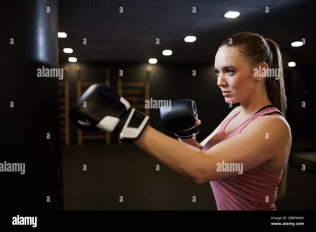Seitenansicht Taille oben Porträt der jungen Frau Boxen mit Stanztasche und lächeln selbstbewusst während des Kampftrainings Stockfoto