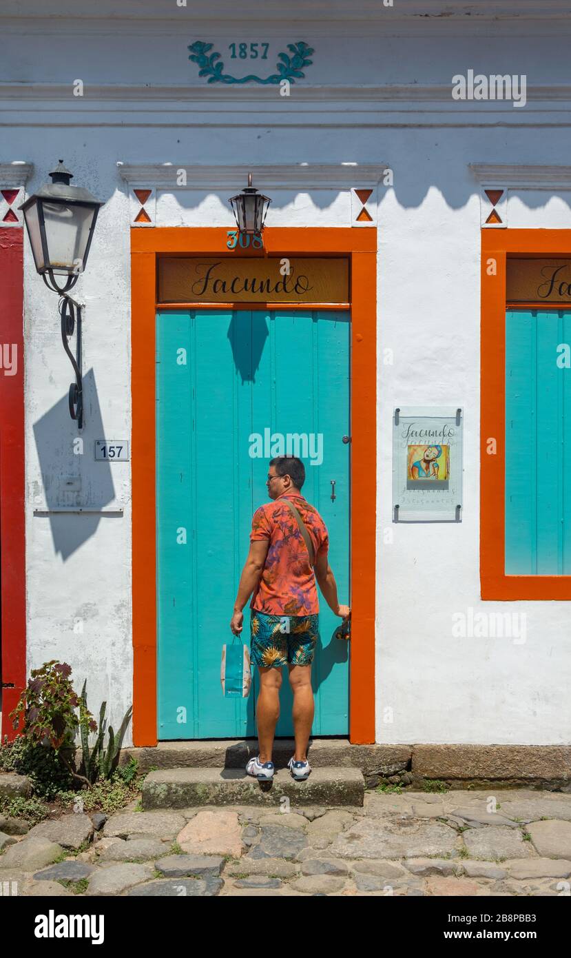 PARATY, RIO DE JANEIRO, BRASILIEN - 28. DEZEMBER 2019: Ein Mann entriegelt die bunte Tür des Gebäudes in der historischen Stadt Paraty, Brasilien. Das erhaltene c Stockfoto