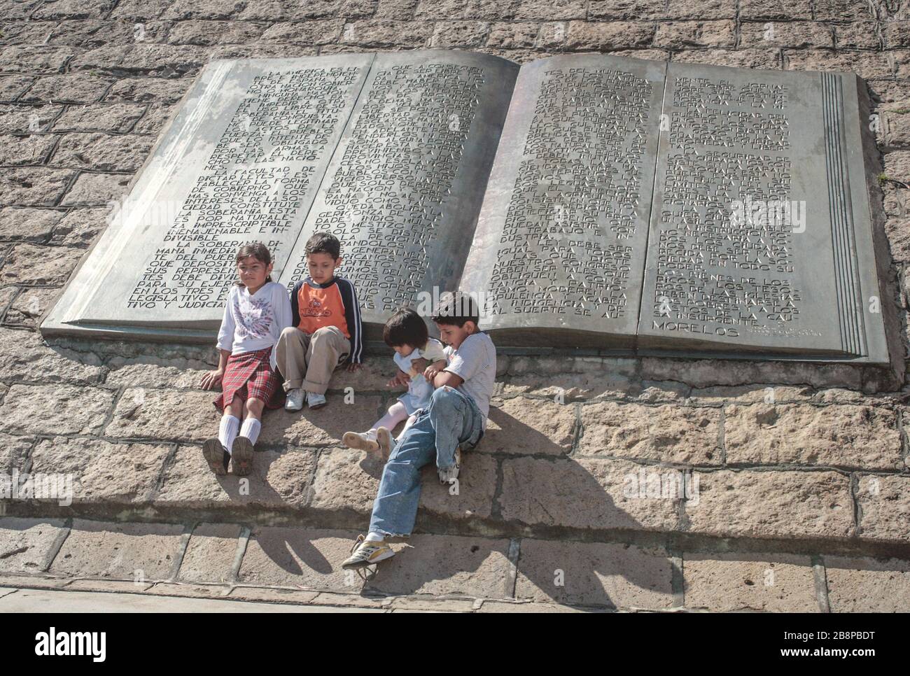 Kinder sitzen neben Buchskulpturen am Sockel des Morelos-Denkmals, Isla de Janitzio, Michoacán, Mexiko Stockfoto