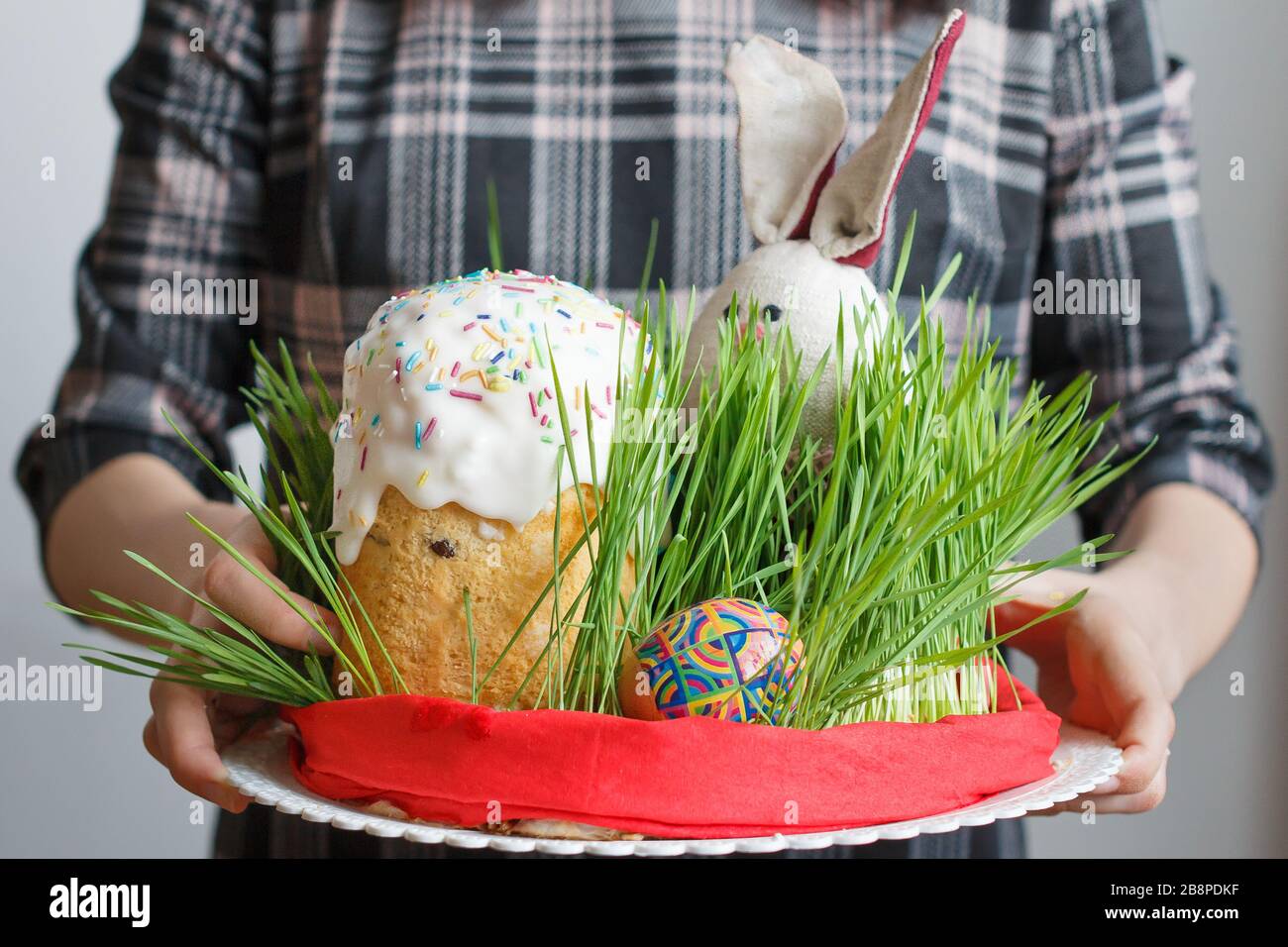 Traditioneller Osterkuchen, Eier und Häschen im Gras in Frauenhand. Osterbrot mit weißer Creme und farbenfroher Dekoration auf der Oberseite. Feasting Stockfoto