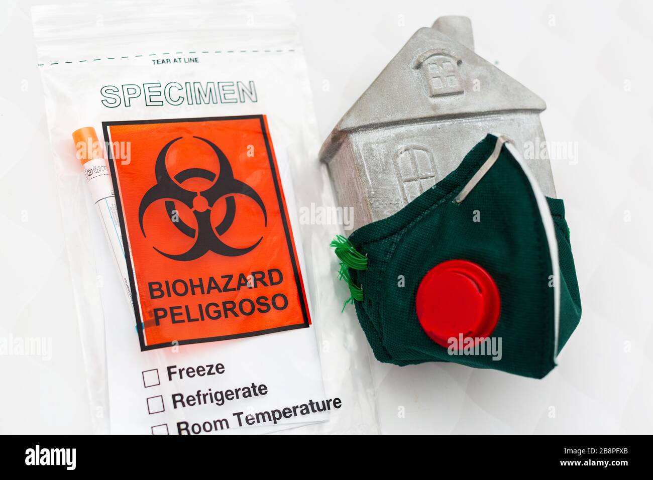Konzept eines Appells, zu Hause zu bleiben. Atemschutzmaske auf einem Spielzeughaus und einem Virus-Test. Stockfoto