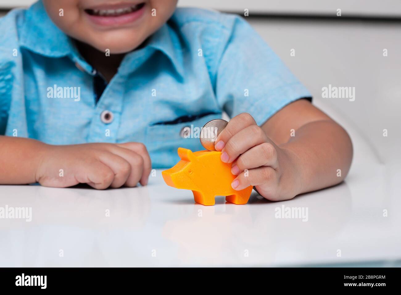 Ein kleiner Junge, der gute motorische Fähigkeiten unter Beweis stellt, indem er eine Münze mit einem Zangengriff hält, bevor er sie in einen kleinen piggeren Bankschlitz legt. Stockfoto
