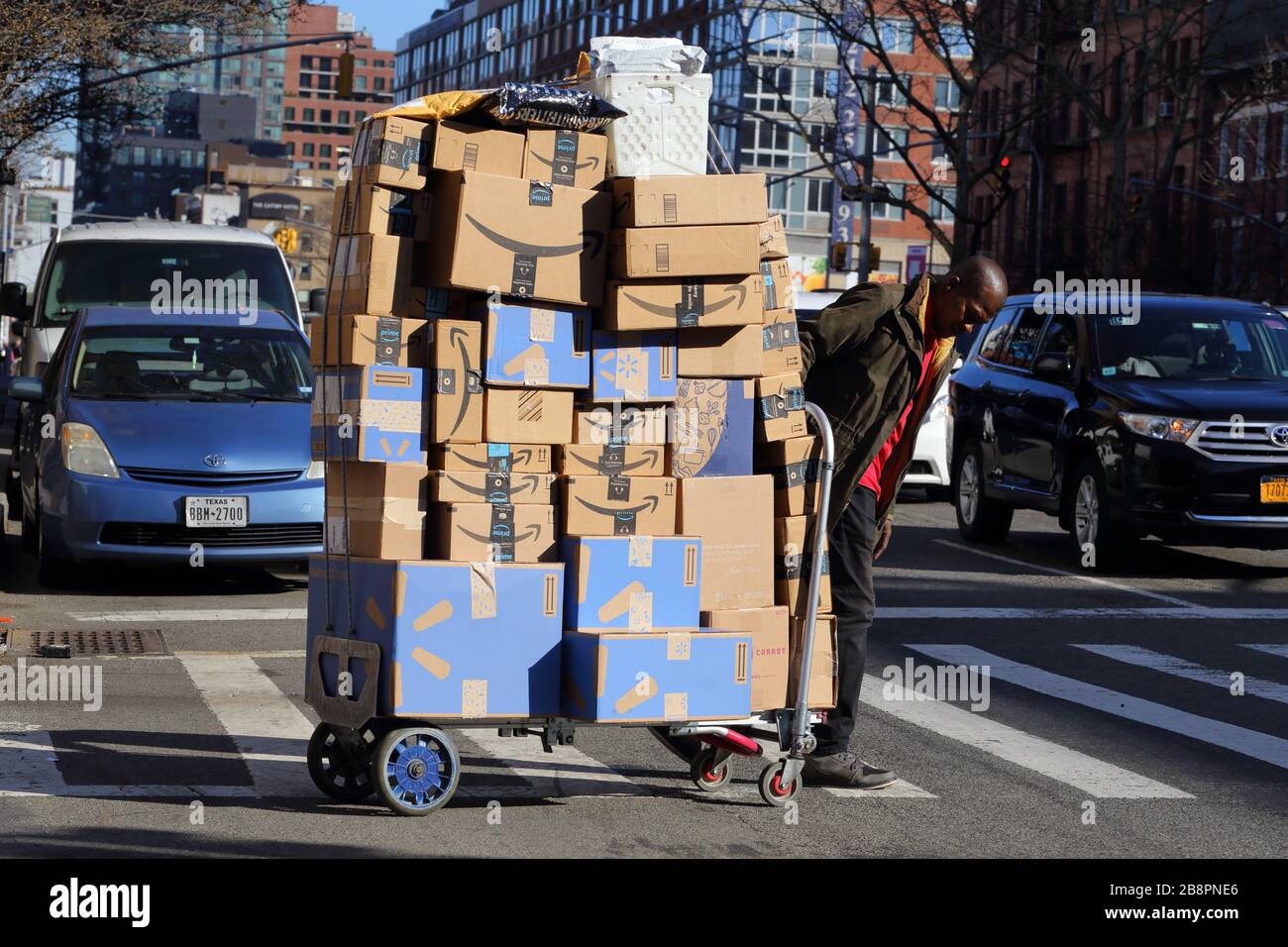 Eine Person zieht einen Handwagen, der mit Kartons und Paketen von Amazon.com und Walmart beladen ist, über eine Straße in New York City. Stockfoto
