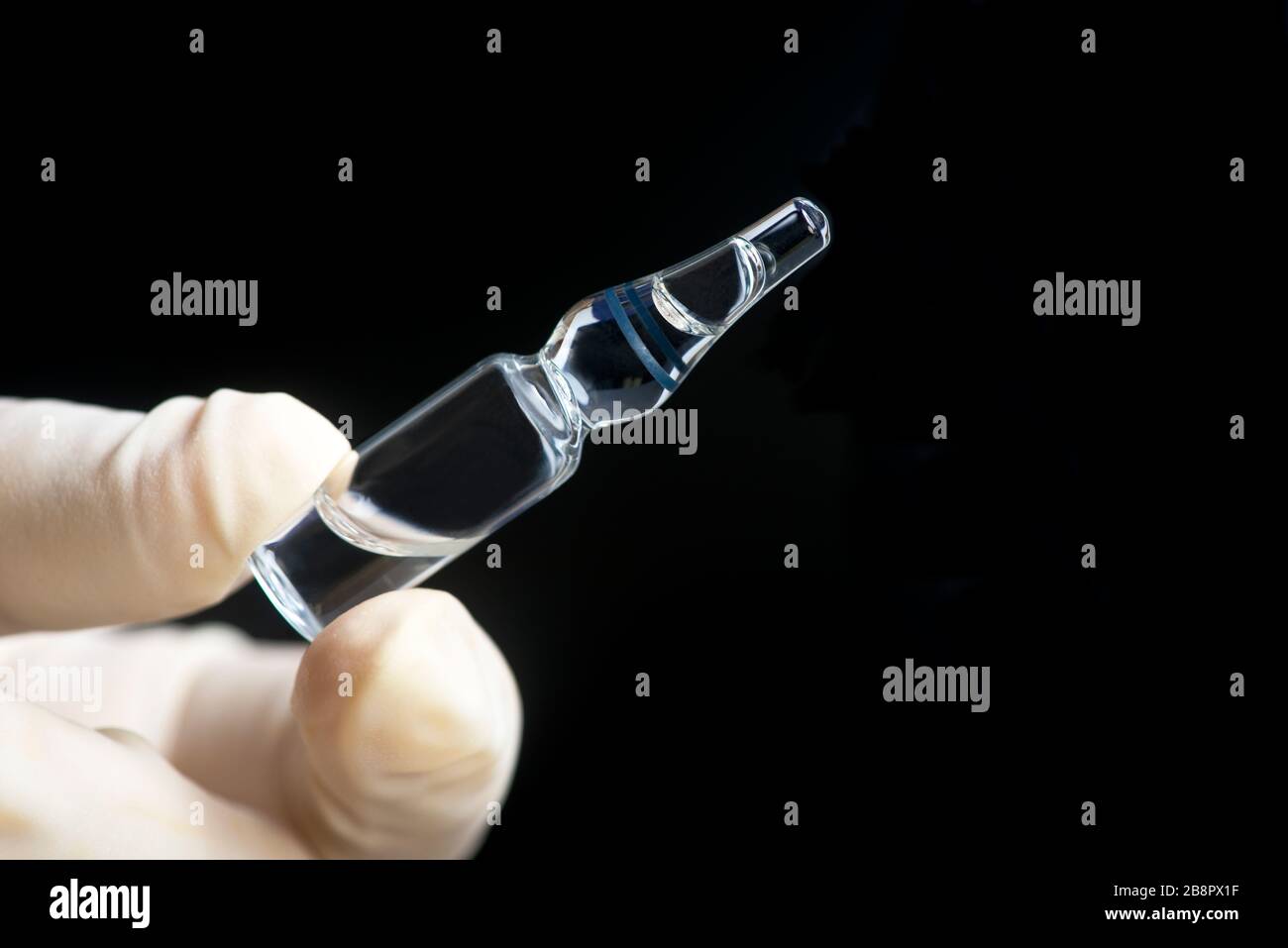 Glaskampule von Medikamenten, die von der Handschuhhand auf schwarzem Hintergrund gehalten werden. Stockfoto