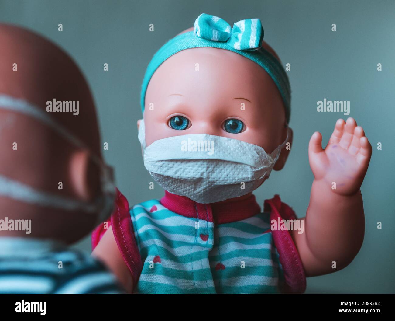Eine Babypuppe mit einer Maske, die Ansteckung darstellt, bei der die verunreinigte Hand angehoben wird, um eine weitere Puppe mit einer Maske zu salutieren Stockfoto