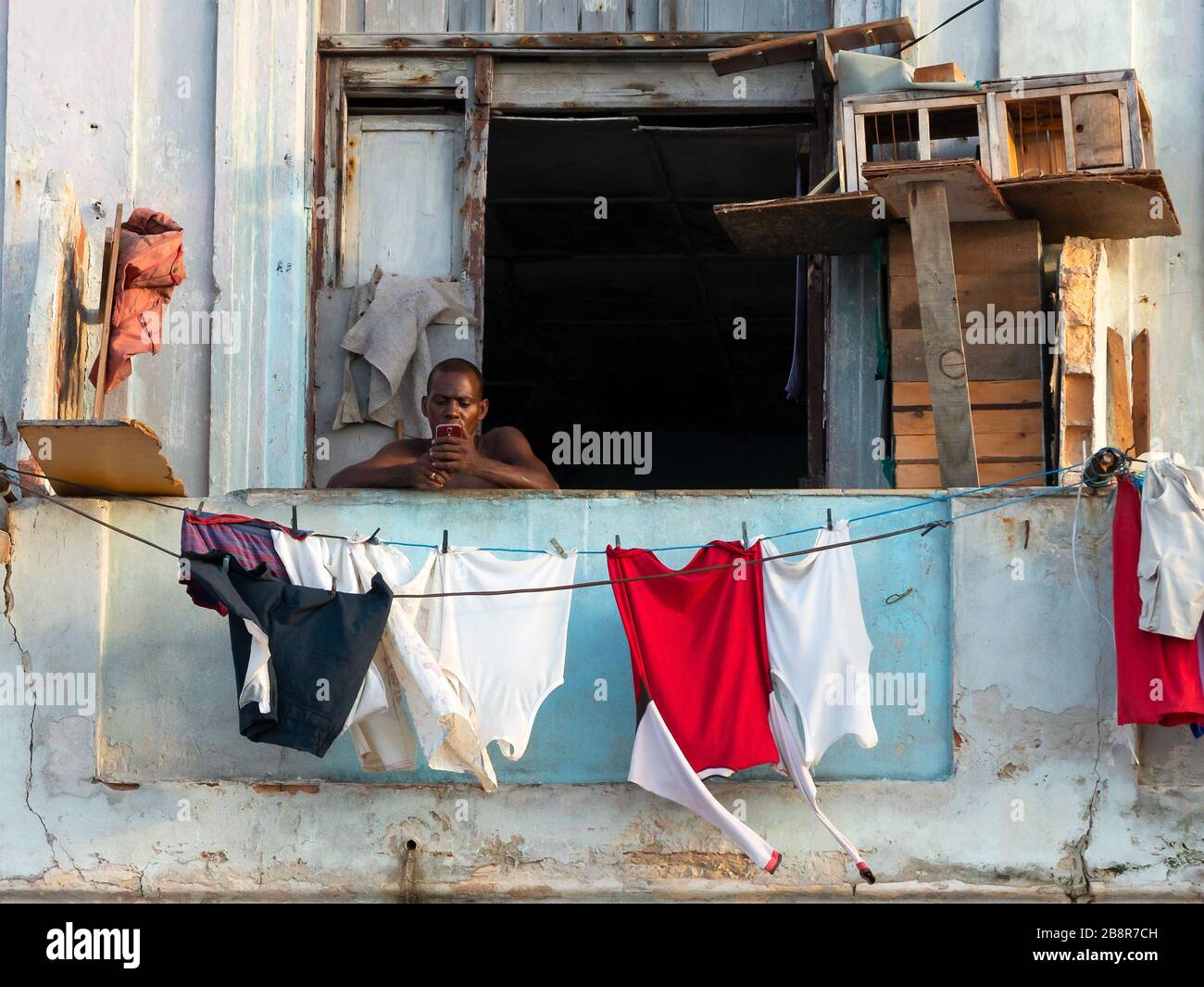 Kubanische Männer auf seinem Balkon, die das Handy zur Kommunikation nutzen. Trotz der schlechten Lebensbedingungen wird das Internet in Havanna, Kuba, beliebter. Stockfoto