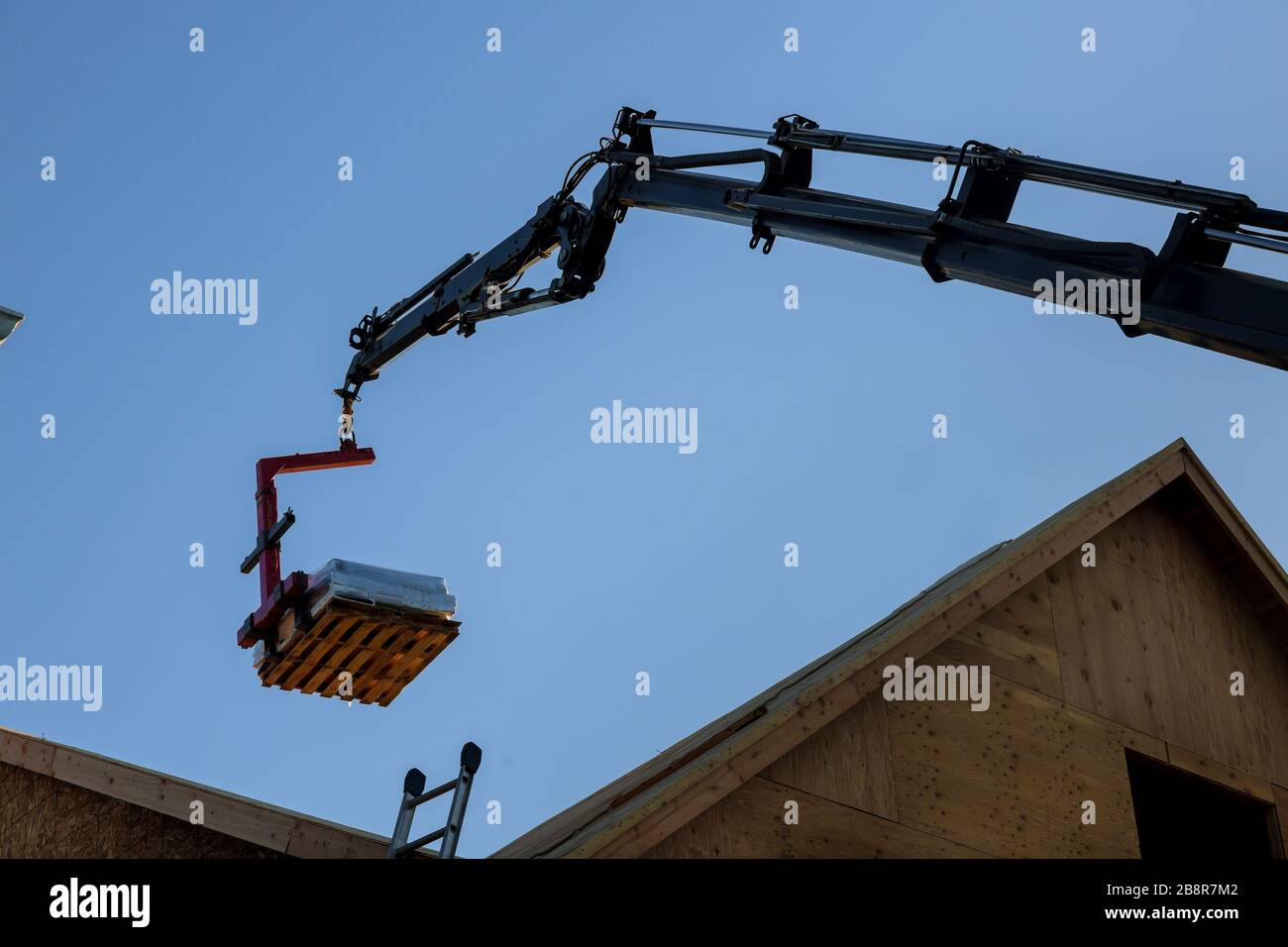 Eine hölzerne Dachstuhl wird von einem Boom Lkw Gabelstapler in das Dach eines neuen Hauses angehoben Stockfoto