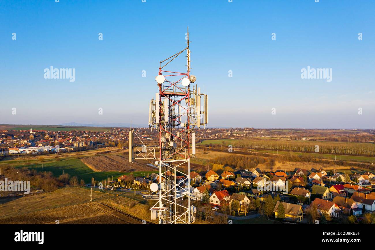 Erhöhter Blick auf einen Zellturm mit Satellitenschüsseln, fernseher, Radio und anderen Telekommunikationsantennen. Die kleine ländliche europäische Stadt wuchert Stockfoto