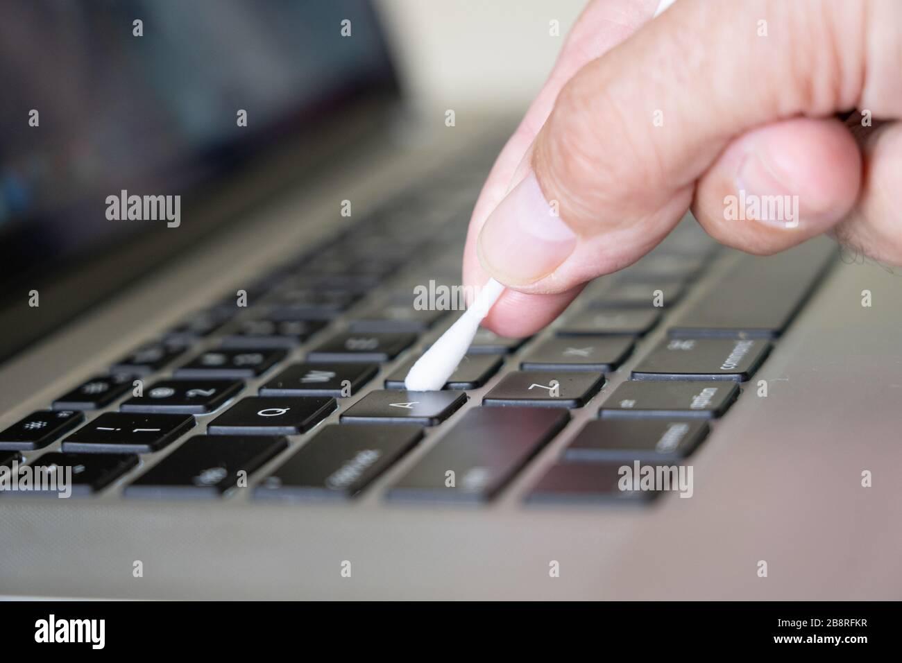 Reinigung einer Computer-Laptop-Tastatur mit einem Wattestäbchen, der während der Coronavirus Pandemie 2020 in eine 70-prozentige Alkohollösung getaucht wurde. Stockfoto