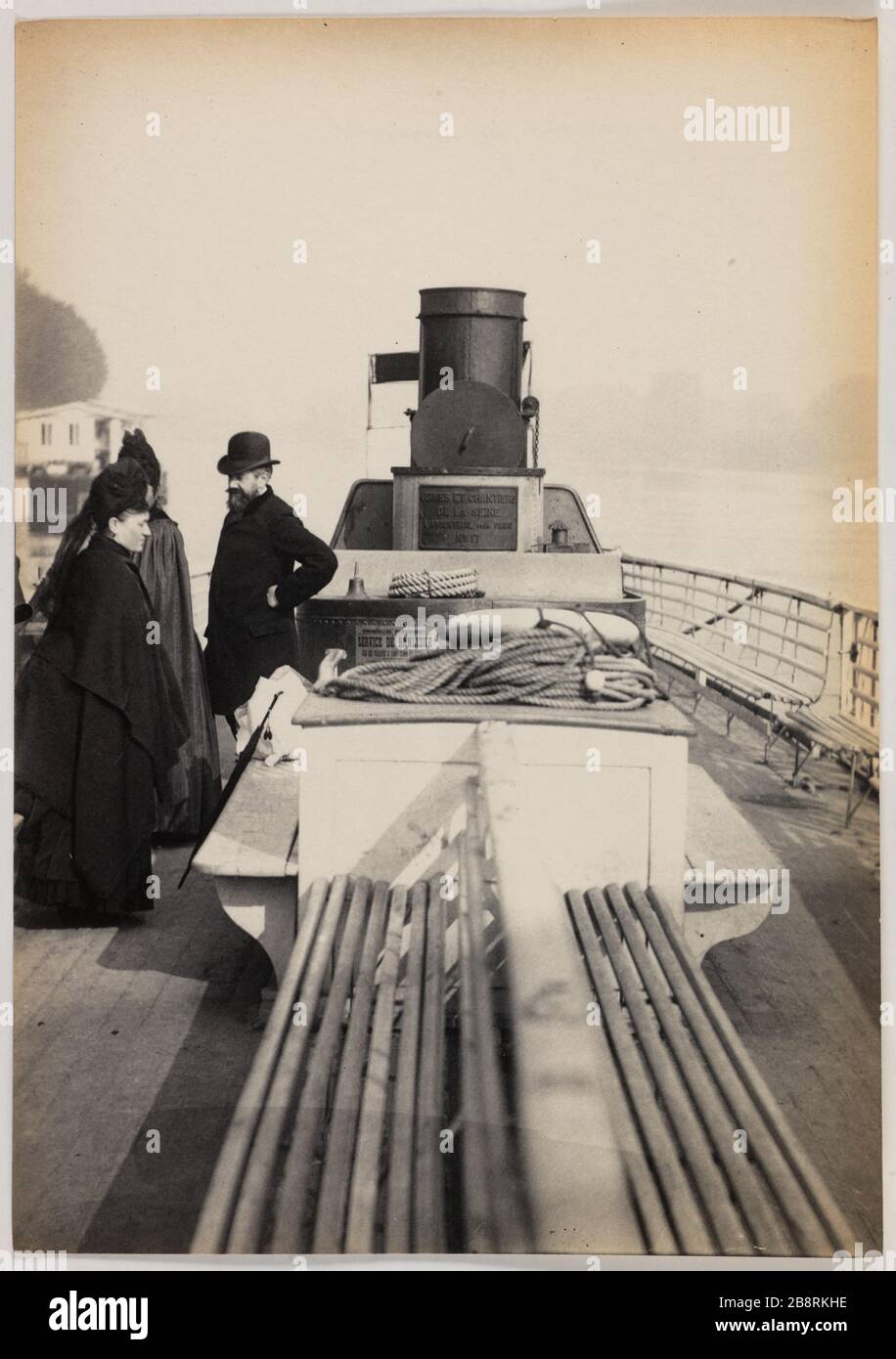 Sèvres / Steamboat Suresnes. Zwei Frauen und ein Mann auf dem Deck eines Dampfschiffs Suresnes Sèvres Blancard, Hippolyte. Sèvres / Bateau à vapeur de Suresnes. 'Deux femmes et un homme sur le pont d'un bateau à vapeur de Suresnes à Sèvres'. Tirage au platine. vers 1890-1890. Paris, musée Carnavalet. Stockfoto