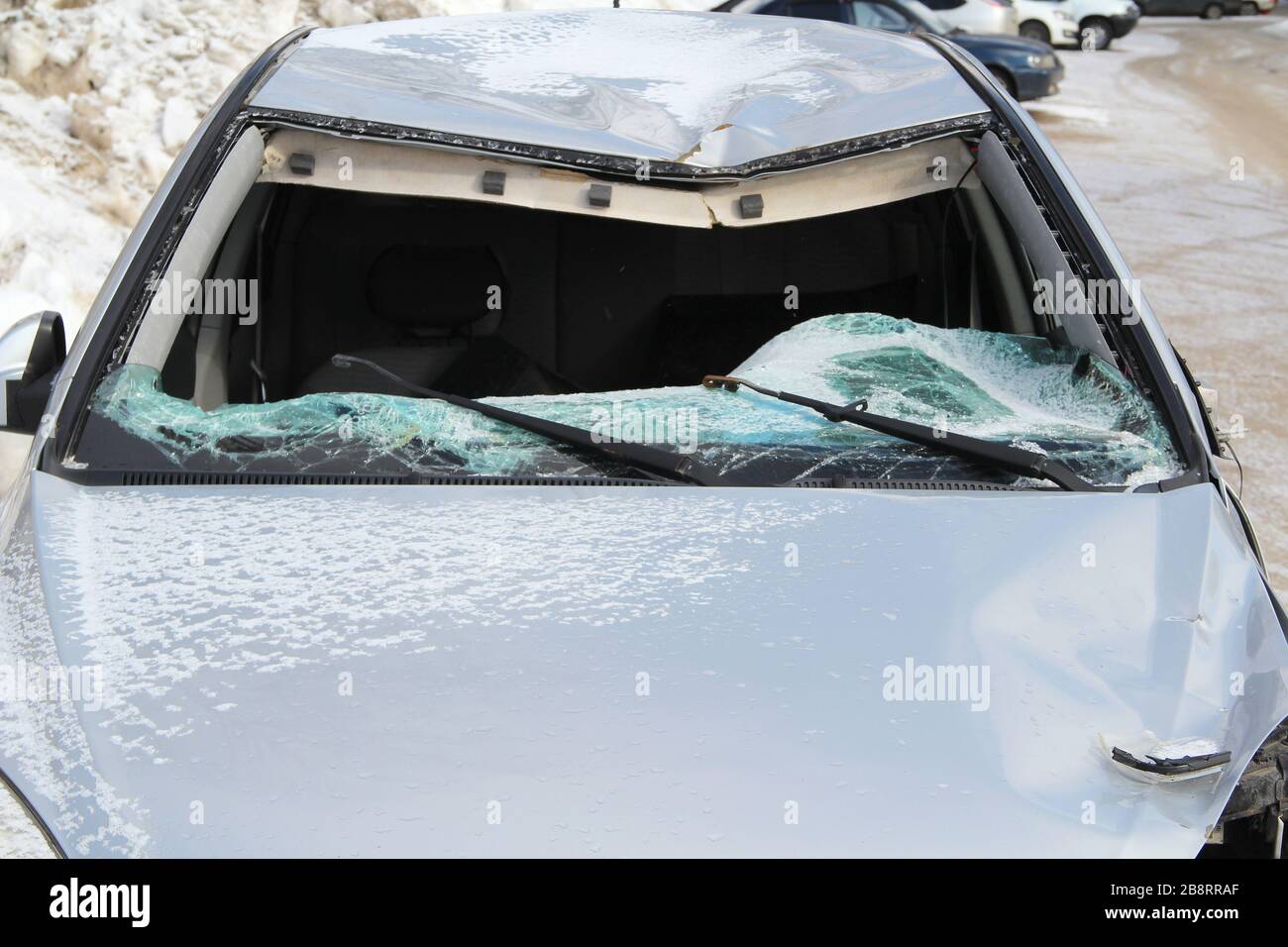 Ein zerbrochenes silbernes Auto nach einem Unfall auf der Straße. Zerbrochene Windschutzscheibe aus nächster Nähe. Verkehrssicherheitskonzept. Stockfoto