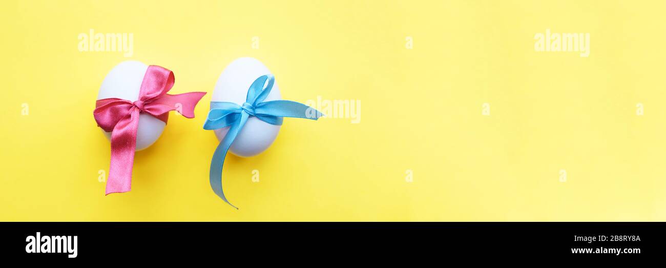 Zwei weiße, in blaue und rosafarbene Bänder gewickelte Eier auf gelbem Hintergrund. Banner. Osterkonzept. Stockfoto