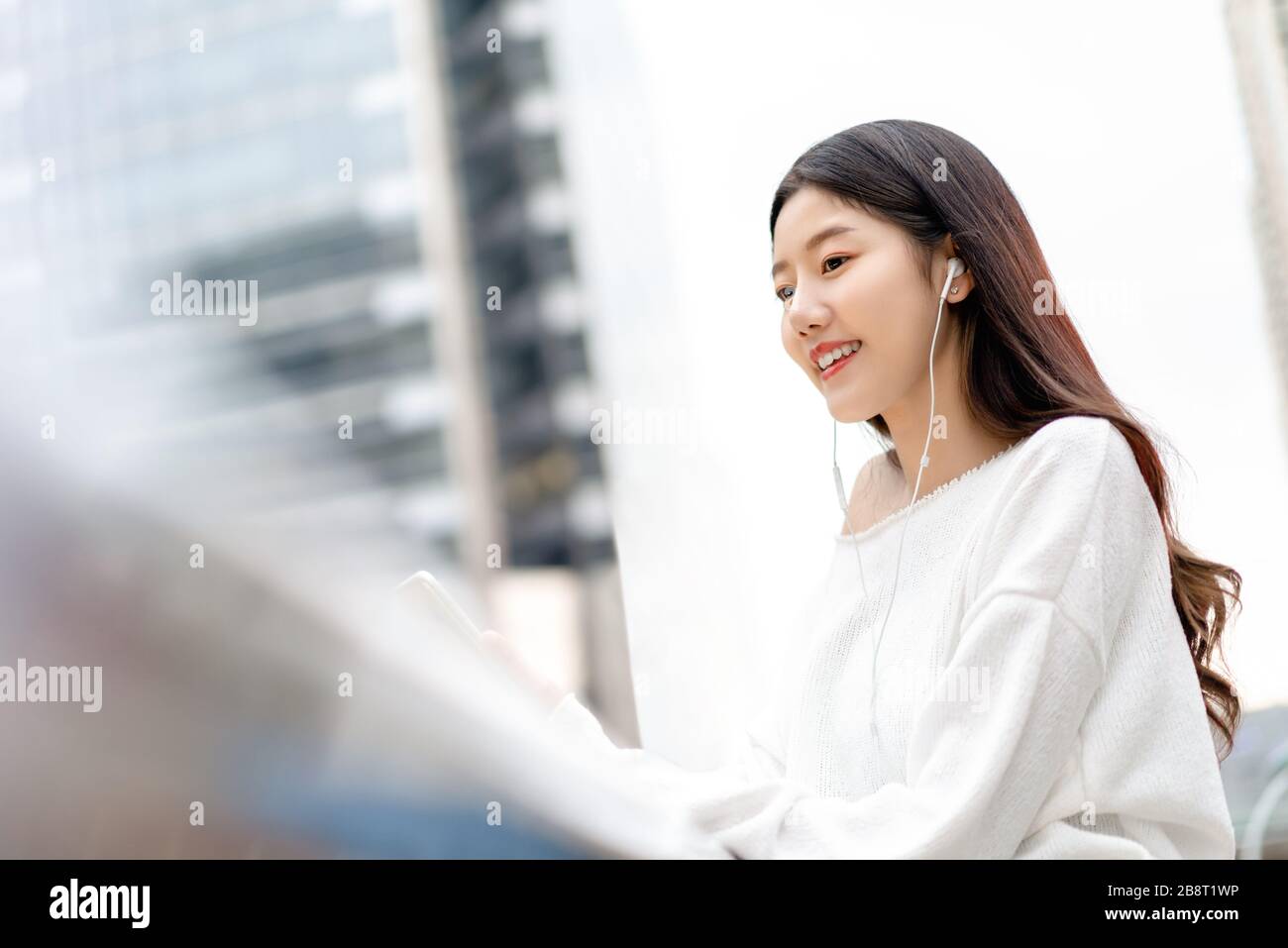 Junges, hübsches asiatisches Mädchen, das Musik auf Ohrhörern in der Stadt hört Stockfoto