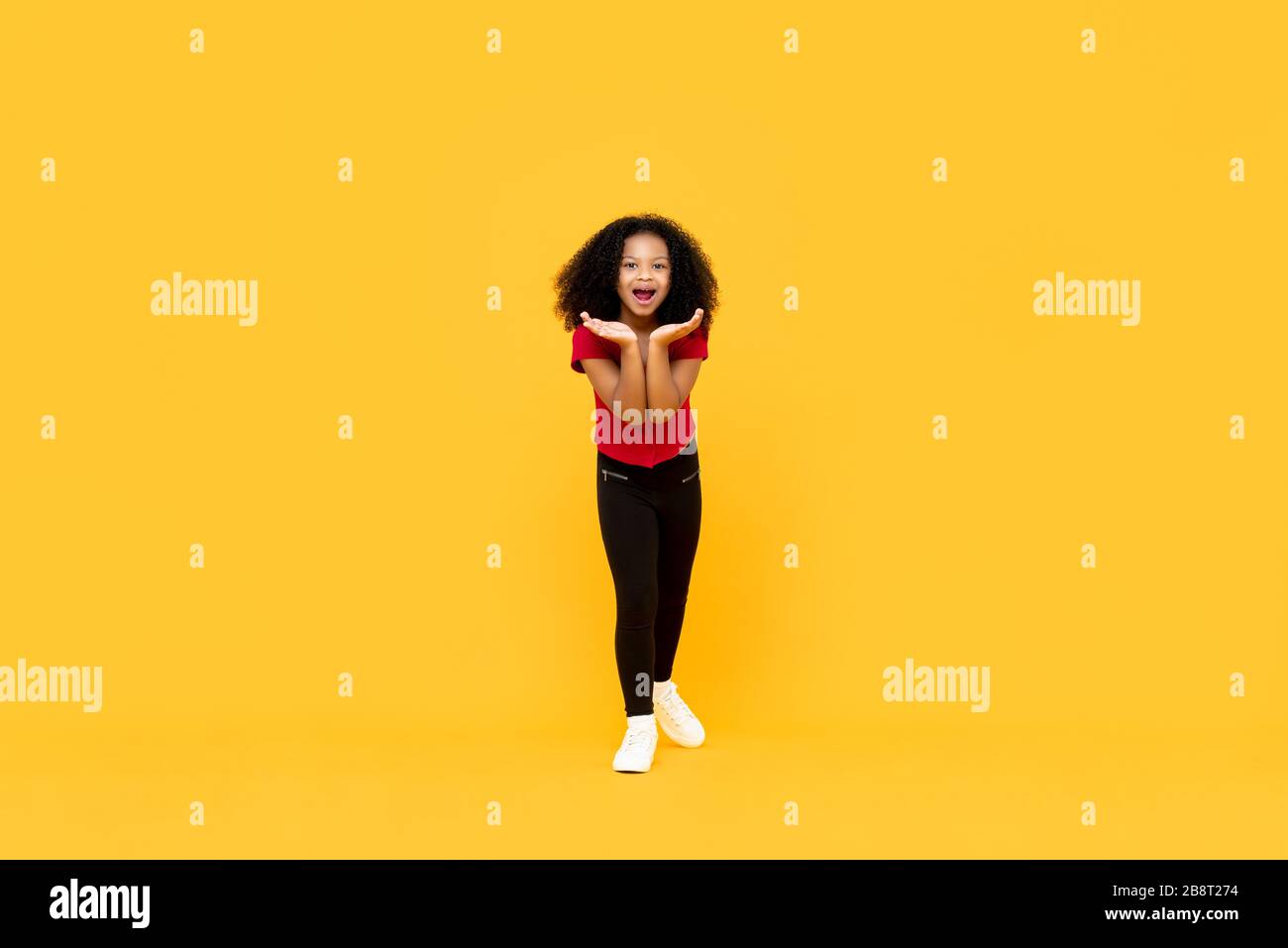 Gemischte Rasse Afro Mädchen in überraschter aufgeregter Geste mit offenen Händen isoliert auf gelbem Hintergrund Stockfoto