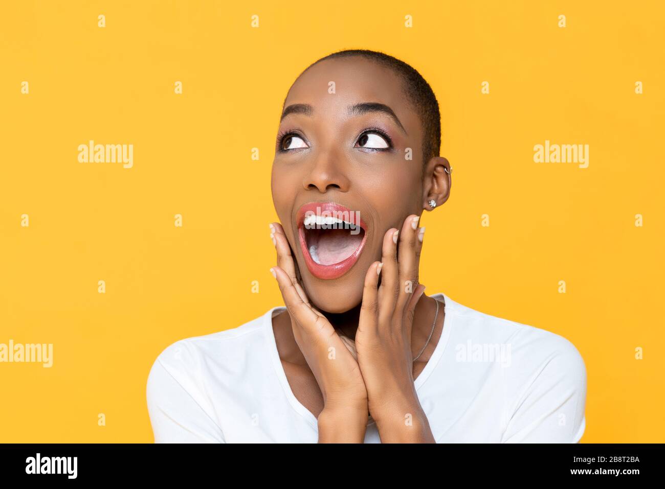 Überraschte die wundervolle afroamerikanische Frau, die auf gelbem Hintergrund knapst und neben dem leeren Raum aufblickt Stockfoto