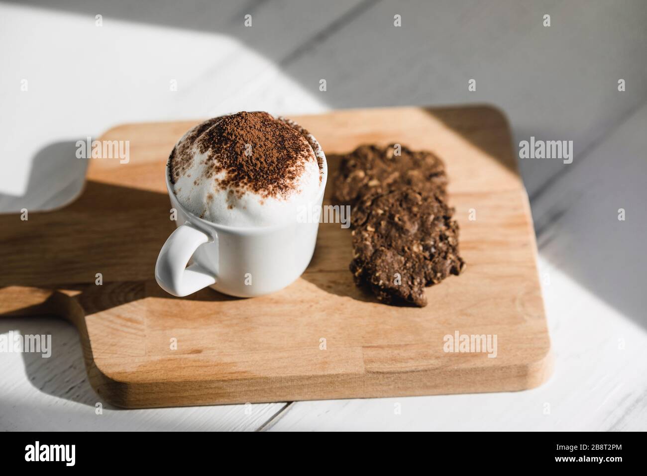 Tasse Babyccino mit dunklen Schokoladenplätzchen auf Holzplatte im Café Stockfoto