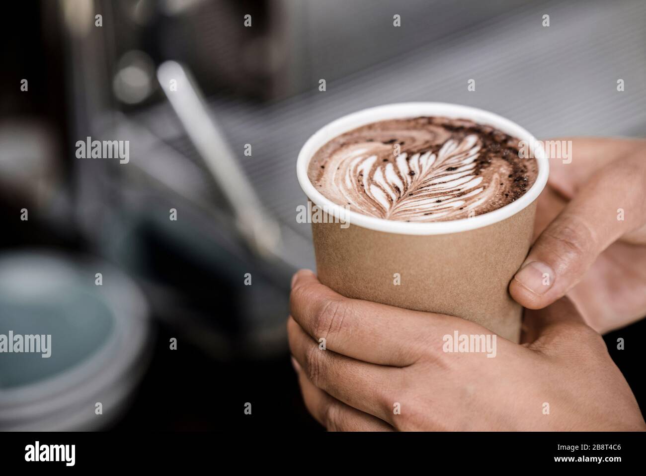 Nahaufnahme der männlichen Hände, die eine Tasse gebrühten heißen Kaffees mit Kunstdesign aus Fern Latte wegnehmen Stockfoto