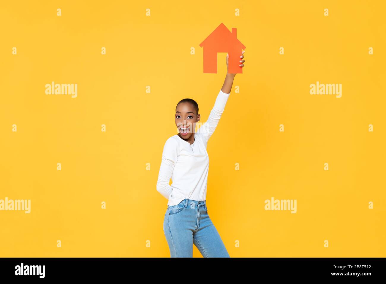 Selbstbewusste lächelnde afroamerikanische Frau, die die Haus-Ikone aufhält, Schnitt in gelb isoliertem Studiohintergrund aus Stockfoto