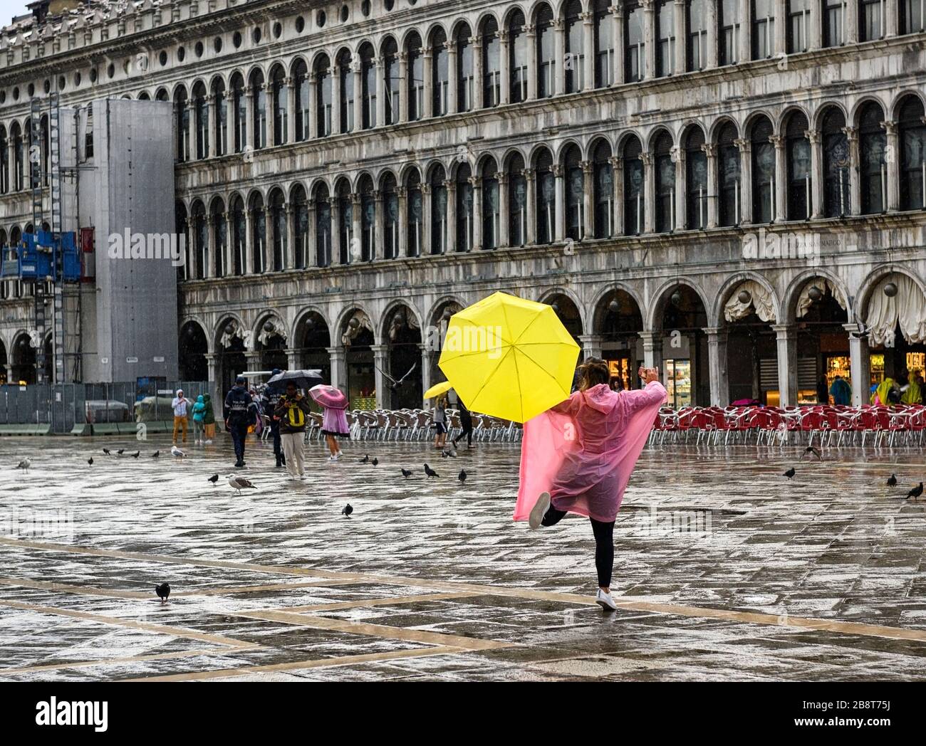 Frauen springen an einem regnerischen Tag in Venedig auf der Piazza in San Marco im Regen Stockfoto Frauen springen an einem regnerischen Tag in Venedig auf der Piazza in San Marco im Regen Stockfoto