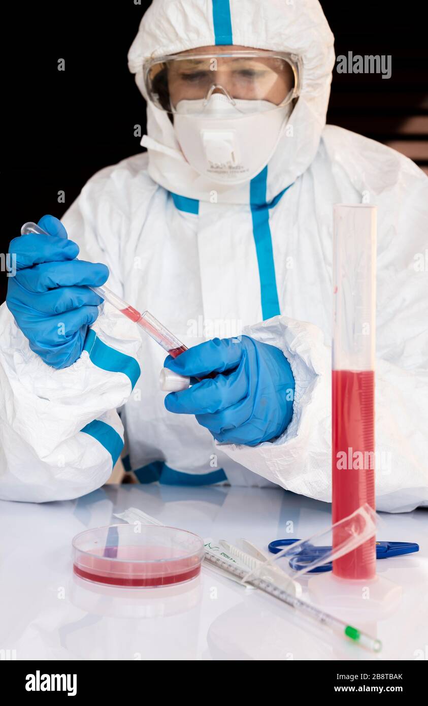 Labortechniker führt Tests durch, um die Ansteckung von Coronavirus Covid-19 zu überprüfen, die vollständig von weißer Gesamt-, Maske-, Handschuhe- und Brille bedeckt ist Stockfoto