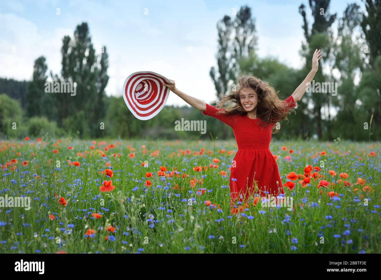 Junge schöne Frau mit erhobenen Armen mit Strohhut im Frühlings-Mohn-Feld. Konzept Freiheit und Glück Sommer Stockfoto
