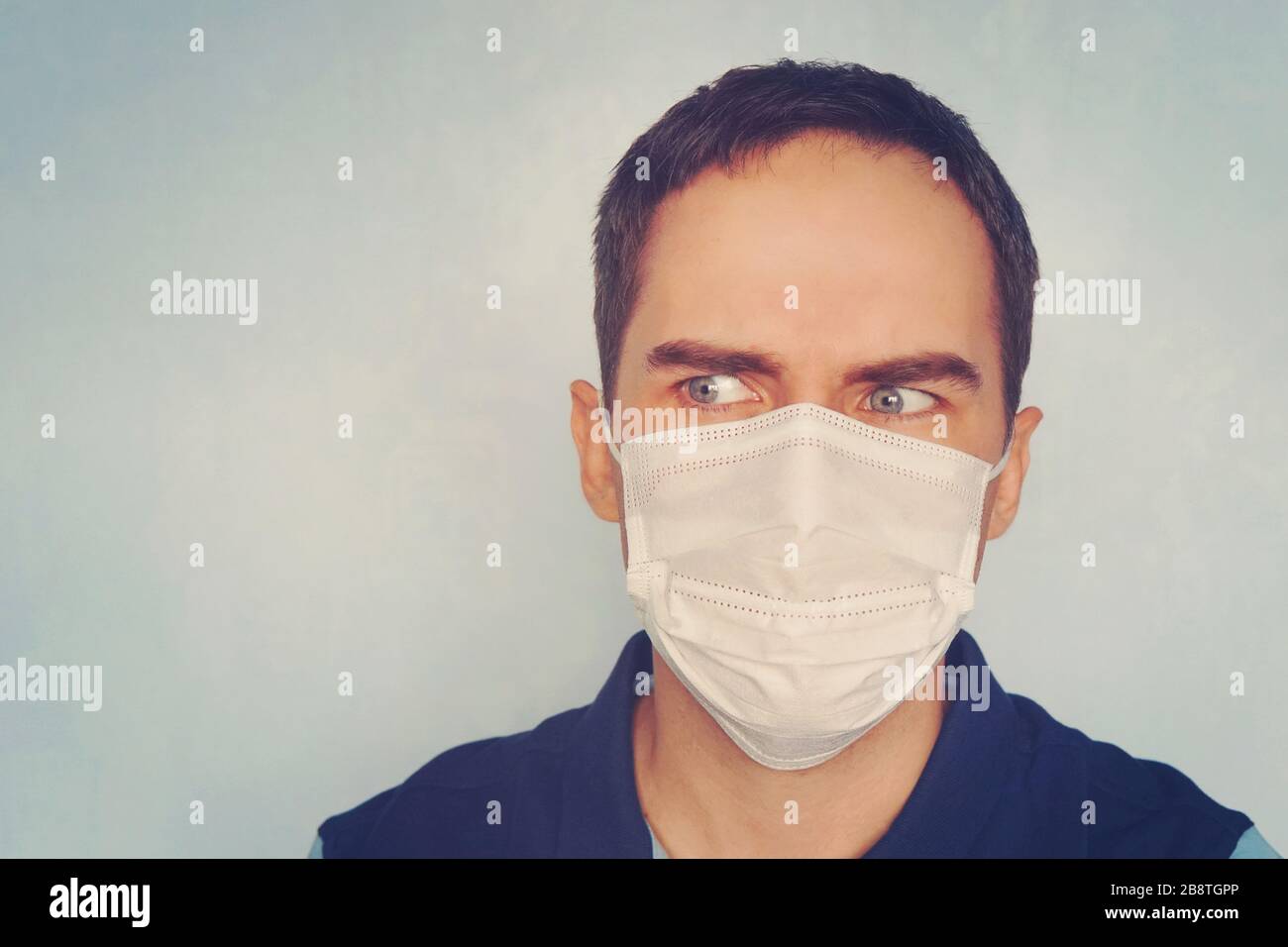 Ein junger Mann in einer weißen medizinischen Atemschutzmaske blickt weg. An der Grippe erkrankt. Schutz vor Keimen. Nachdenklicher Patient. Stockfoto