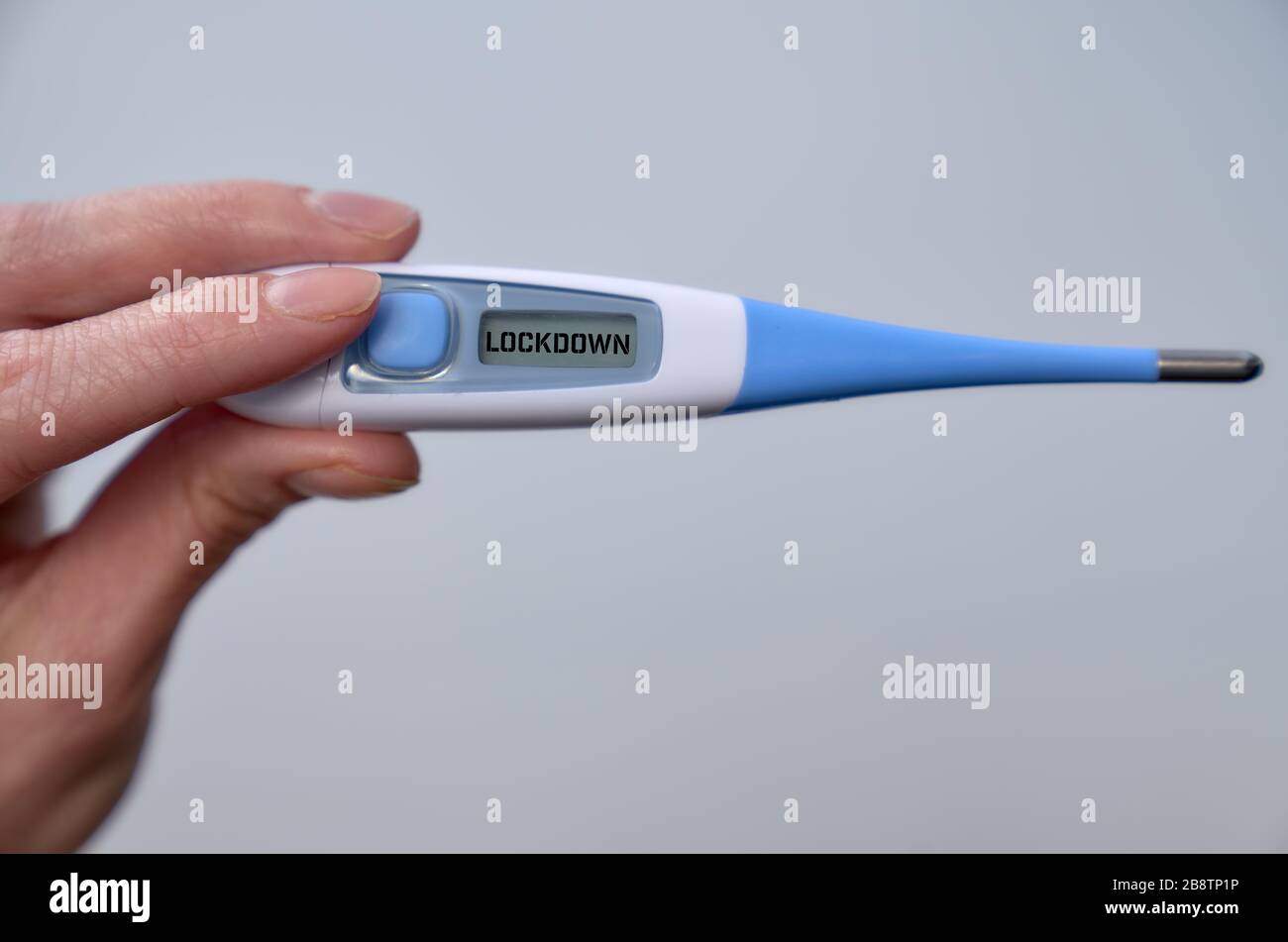 Weibliche Hand hält klinisches Thermometer mit Sperrtext auf dem Bildschirm während der globalen Kovid-19- oder Corona-Pandemie. Stockfoto