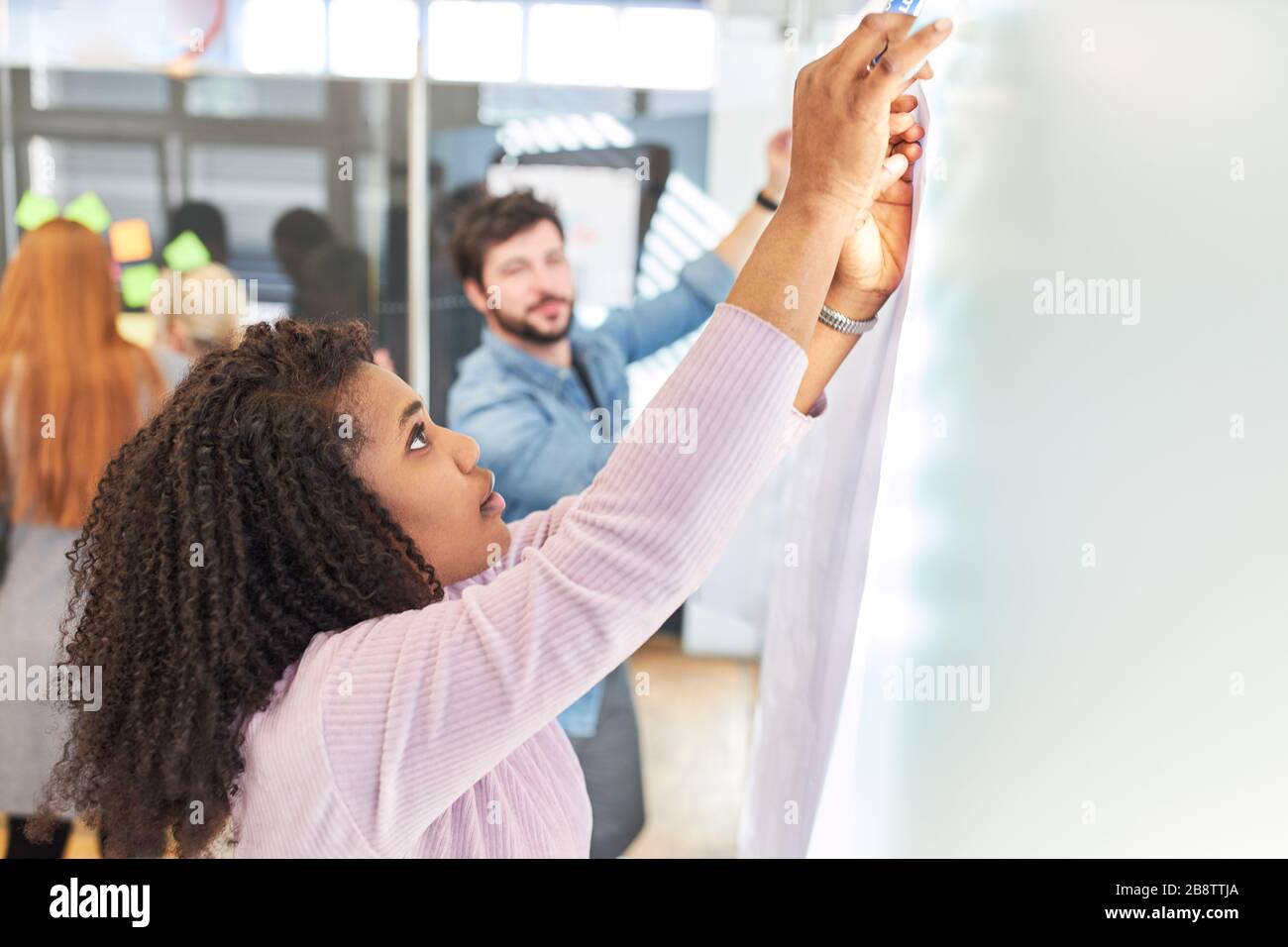 Zwei junge Geschäftsleute oder Studenten bauen im Büro eine Nachrichtentafel auf Stockfoto