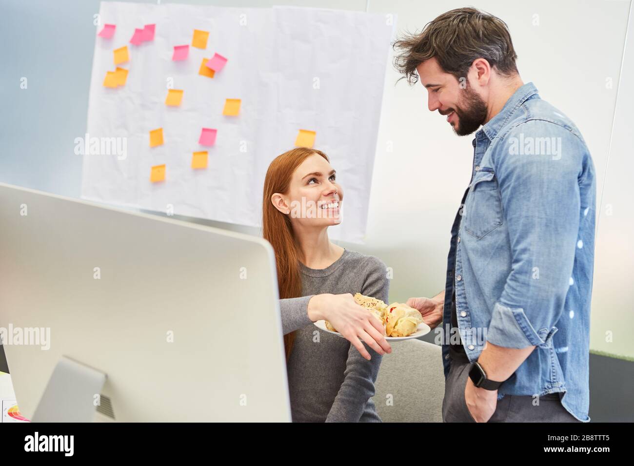 Der Business man bringt einem Kollegen einen Teller Snacks an den Büroarbeitsplatz Stockfoto