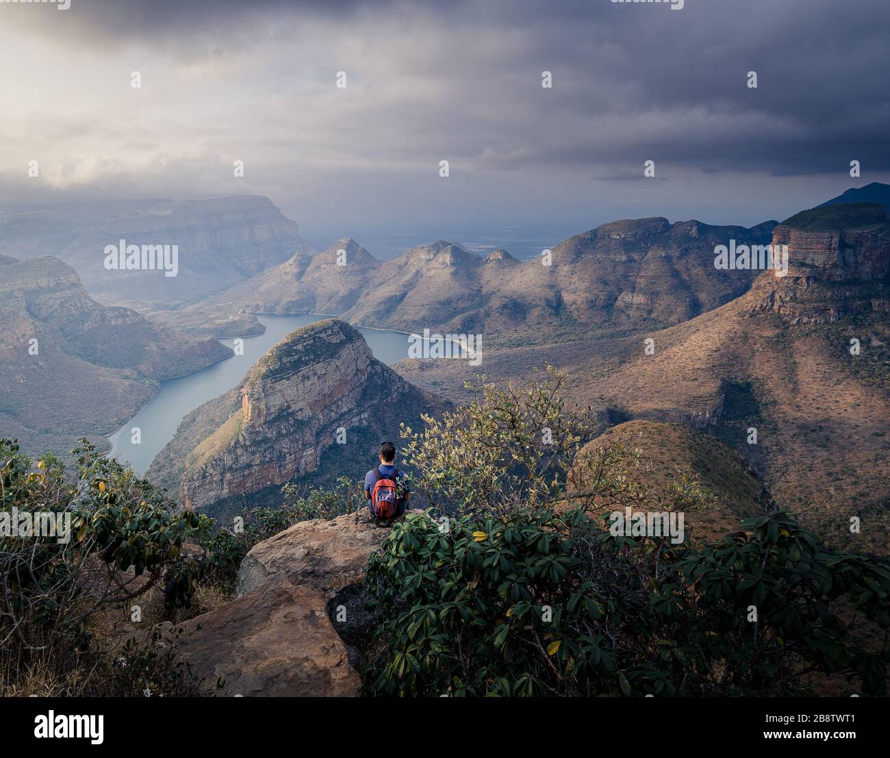 Kaukasischer Mann, der auf einer Klippe sitzt und einen atemberaubenden Blick auf 3 rondavels vom erhöhten Punkt an Mpumalanga Südafrikas Panorama-Panoramastraße bewundert Stockfoto