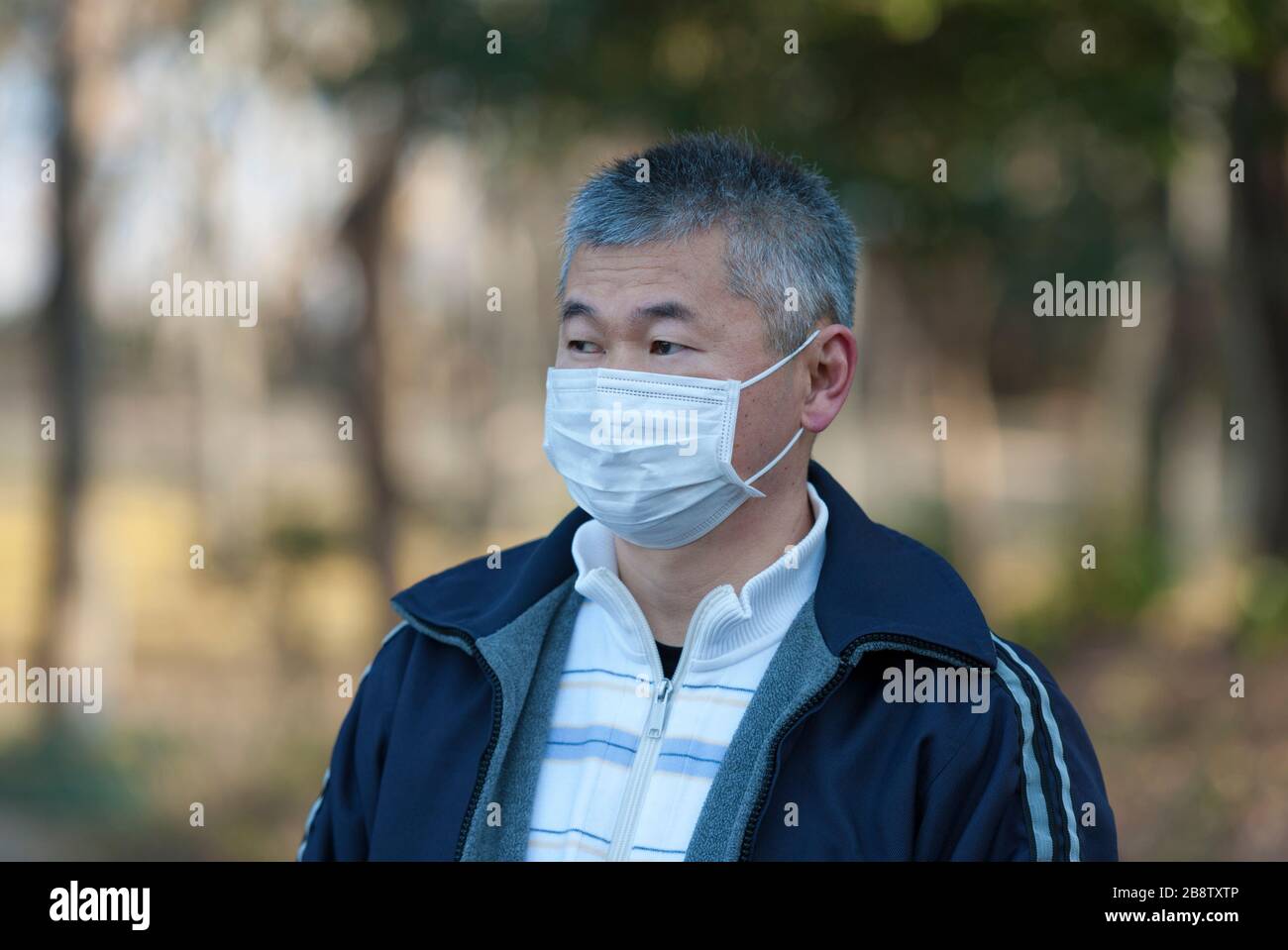 Asian man 50-59 Jahre alt im Freien mit weißer Maske zum Schutz vor Viren, Grippe, Heuschnupfen und anderen Krankheiten. Blick zur Seite. Stockfoto