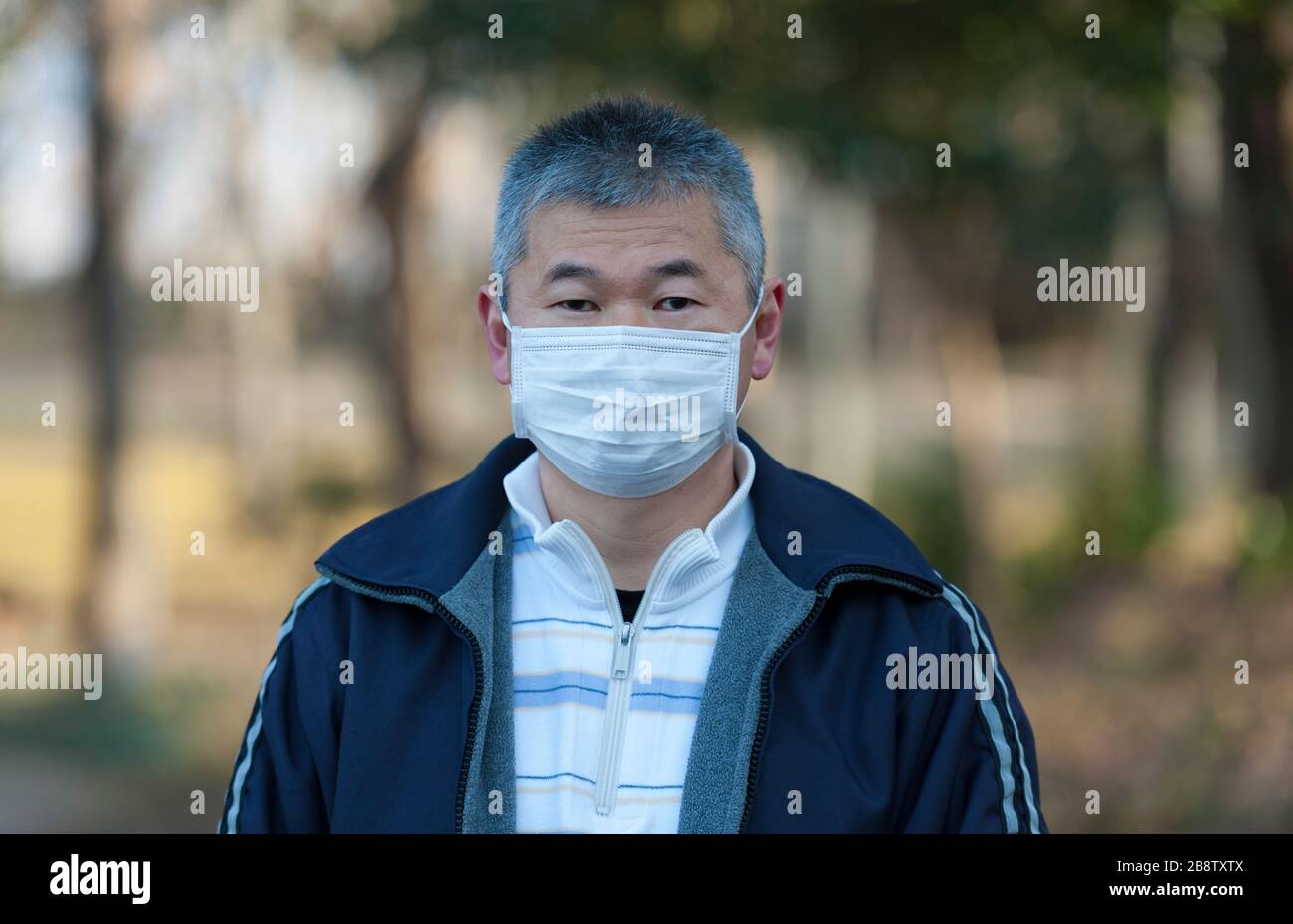 Asian man 50-59 Jahre alt im Freien mit weißer Maske zum Schutz vor Viren, Grippe, Heuschnupfen und anderen Krankheiten. Blick auf die Kamera. Stockfoto