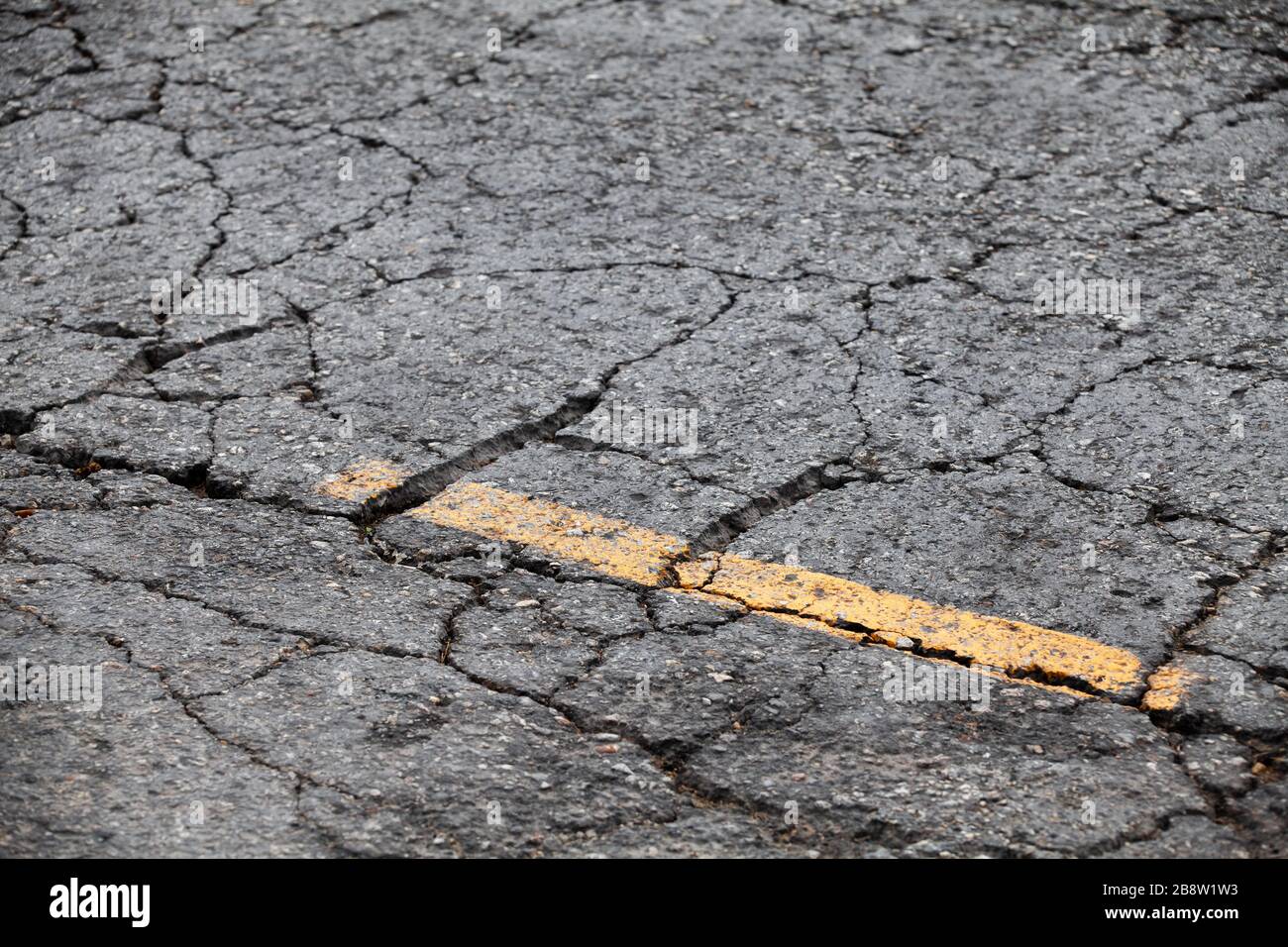 Gerissene Asphaltstraße mit gelber Trennlinie. Abstrakte Hintergrundtextur für den Transport Stockfoto