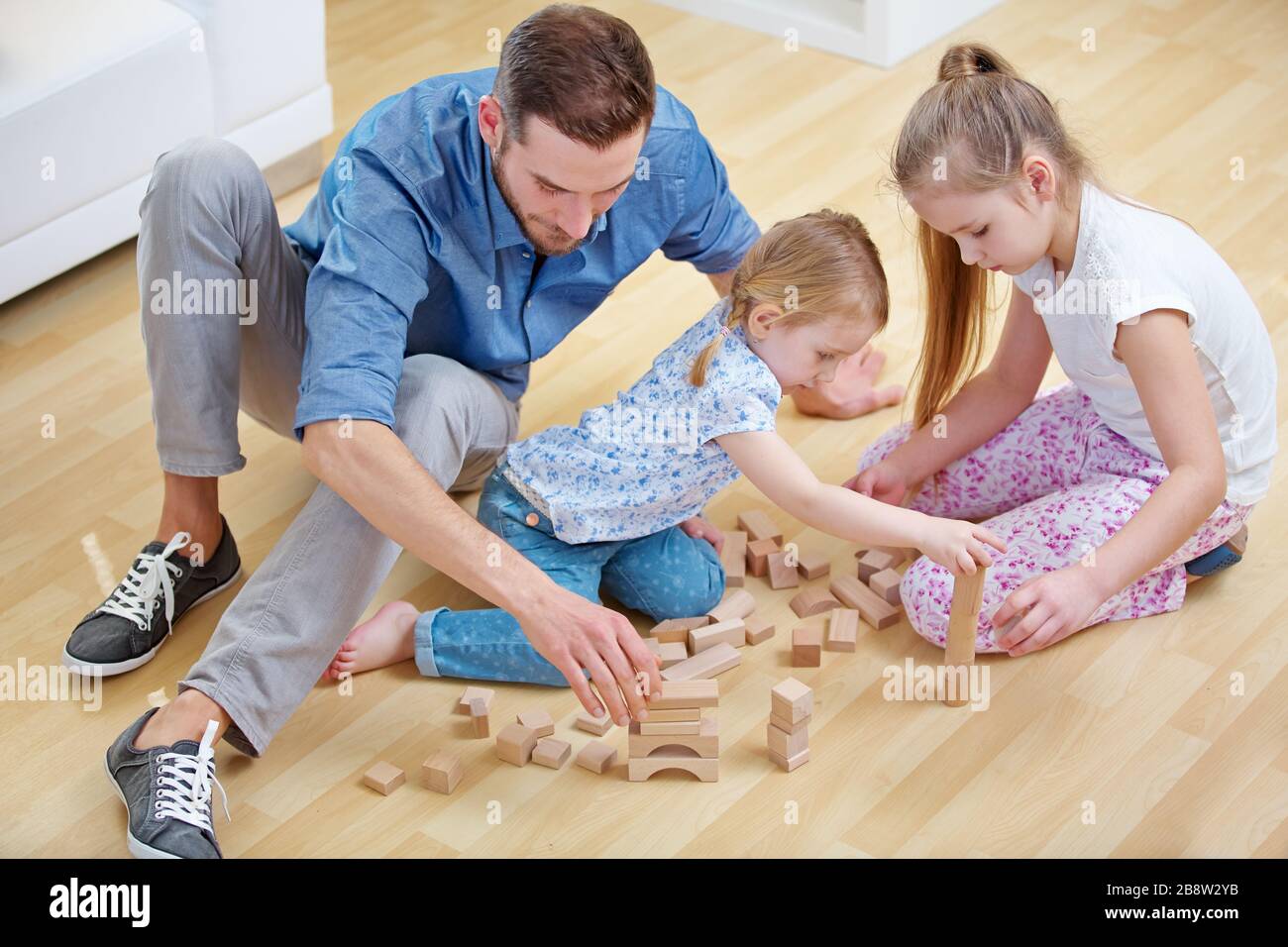 Familie mit Vater und zwei Kindern spielt zu Hause mit Bausteinen zusammen Stockfoto