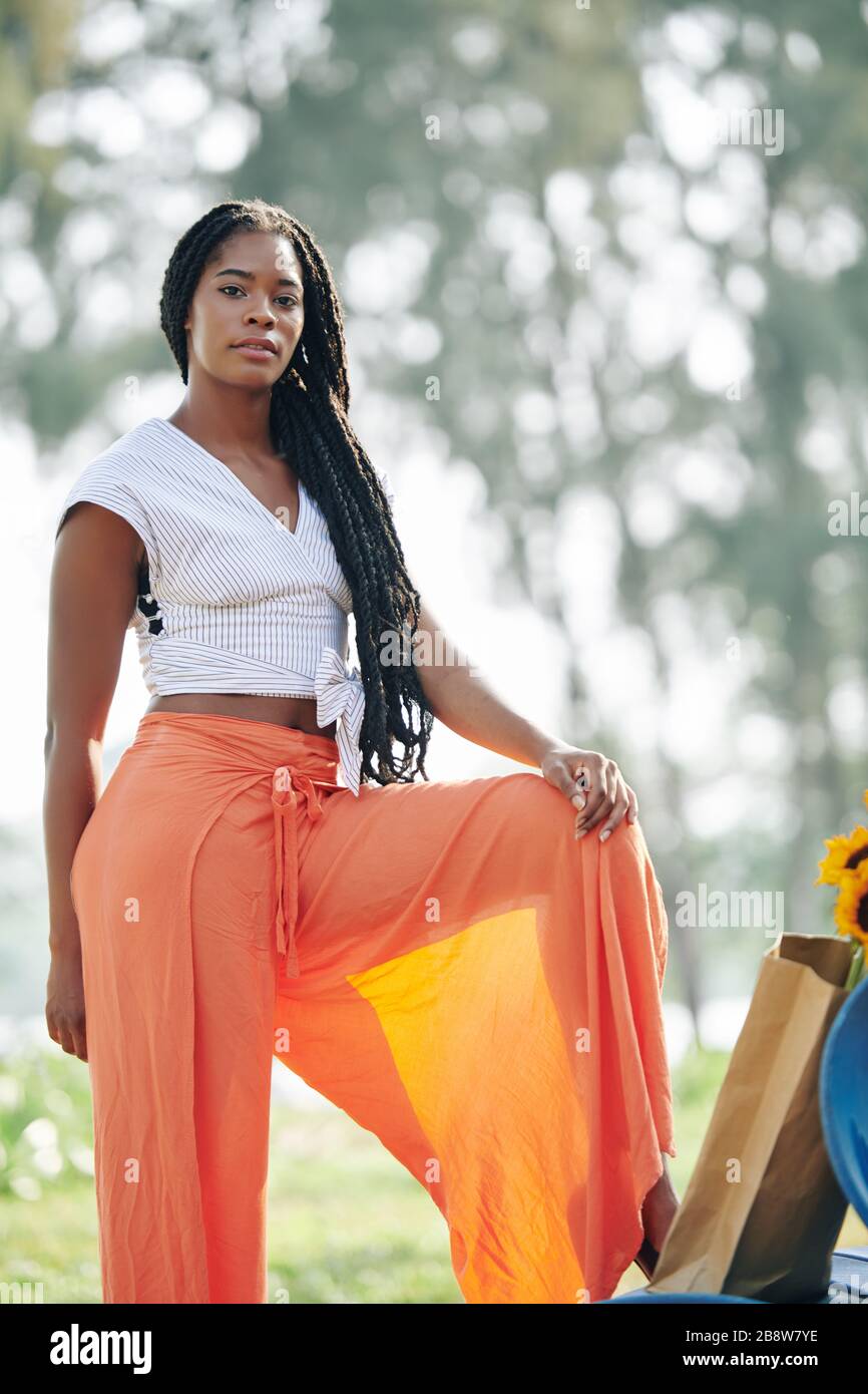 Schöne seriöse junge Frau, die im Freien in einer breiten orangefarbenen Leinenhose posiert Stockfoto