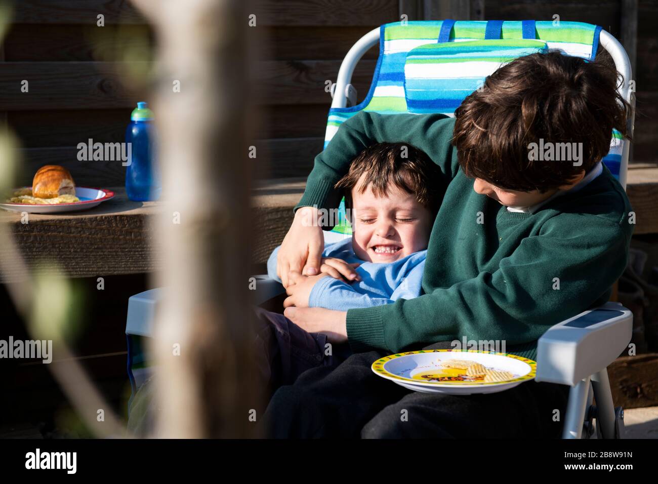 Nahaufnahme von zwei Jungen, die in einem zusammenklappbaren Camping-Stuhl sitzen und grinsen. Stockfoto