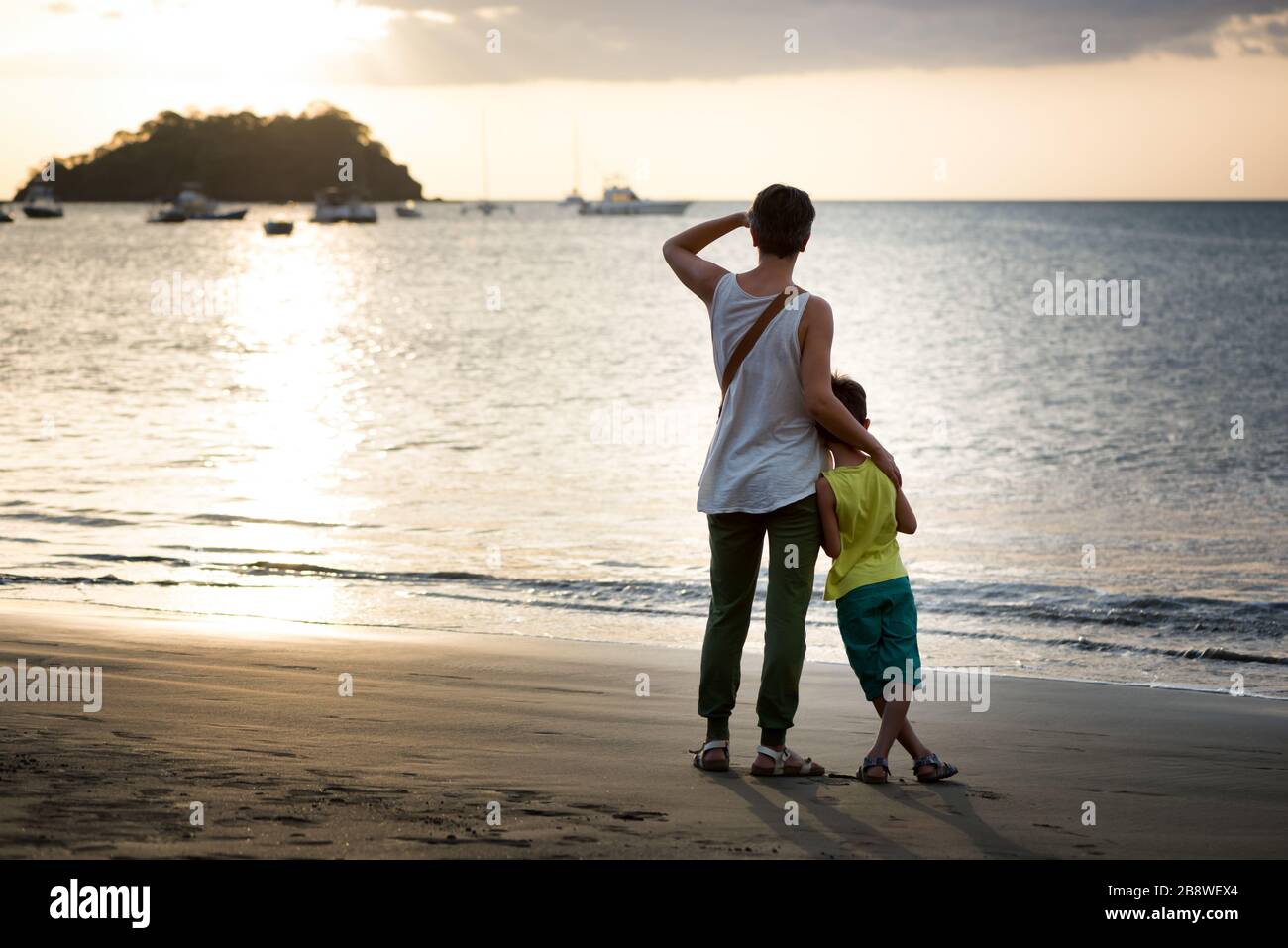Mutter und Sohn blicken bei Sonnenuntergang vom tropischen Strand auf das Meer. Konzept der Liebe und des Urlaubs. Stockfoto