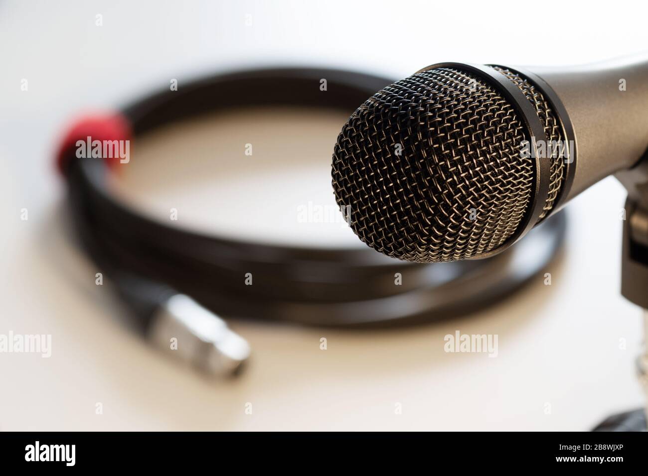 Nahaufnahme des Mikrofonkopfs mit schwarzem Gitter und Kabel mit xlr-Anschluss im Hintergrund isoliert auf weiß. Musik, Audio, Hi-Fi, Karaoke und Soun Stockfoto