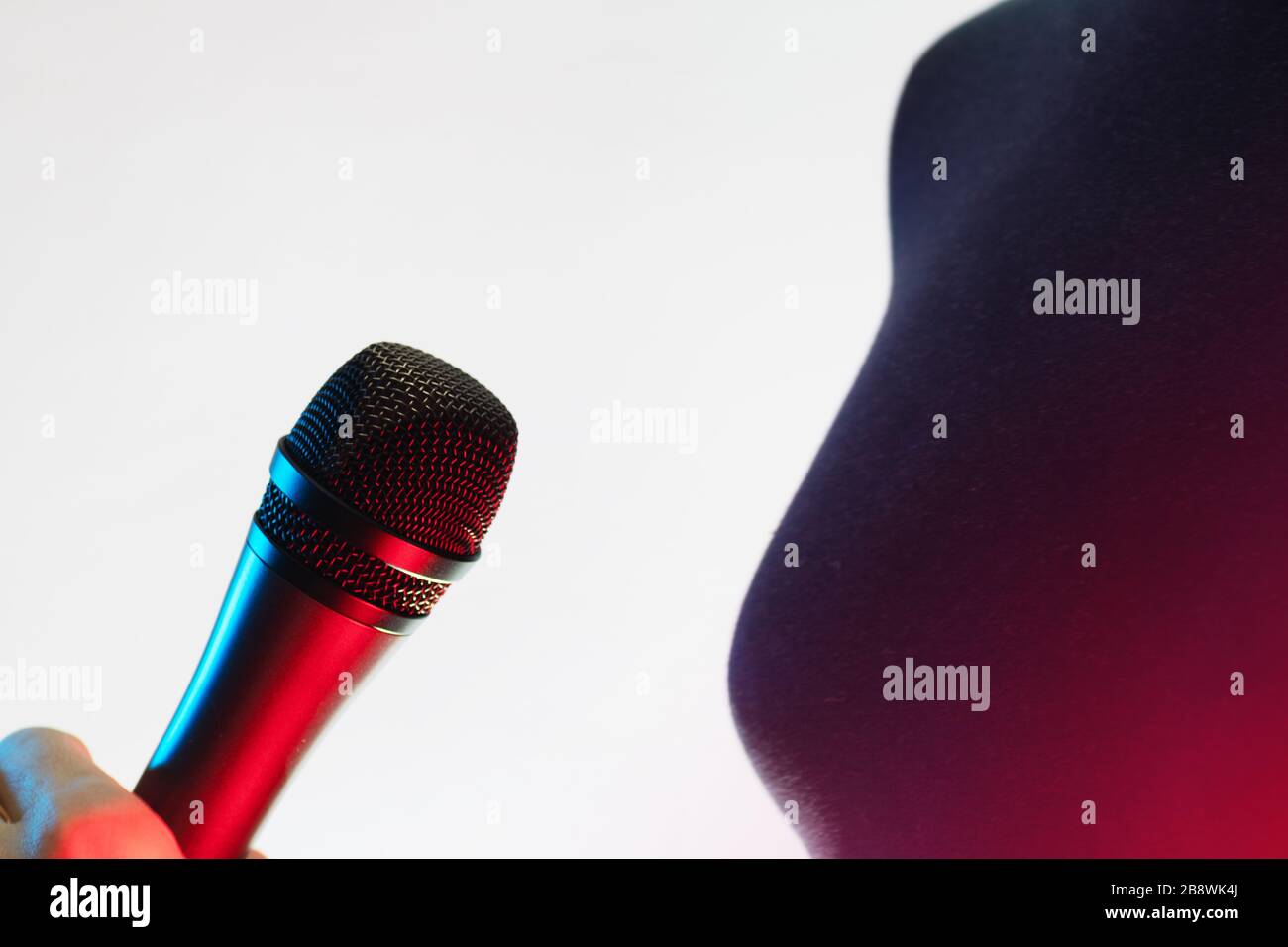 Nahaufnahme der Frau, die ein blau-rot beleuchtetes Stimmmikrofon auf weißem Hintergrund hält. Musik, Gesang, Disco, Karaoke und Tonwiedergabe. Stockfoto